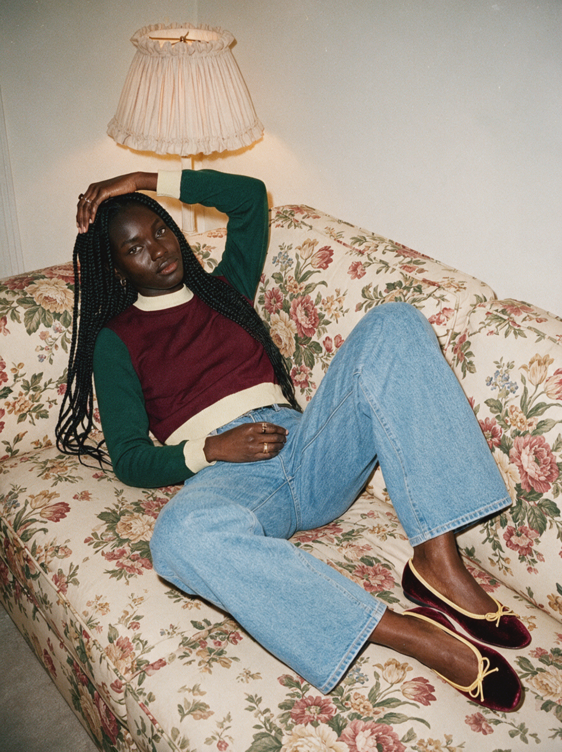 Woman in a knit sweater vest and jeans lounging on a floral sofa beneath a lamp