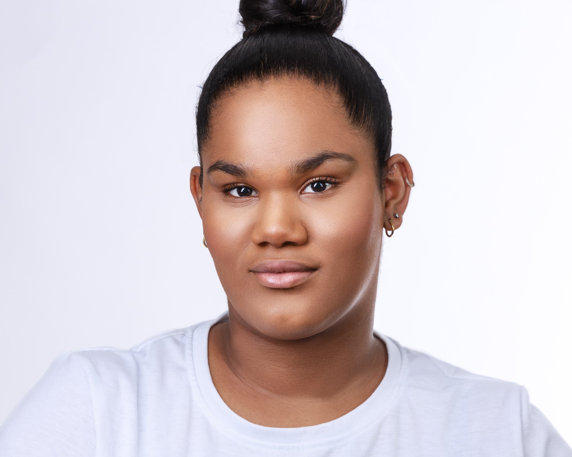 Portrait of a young person with a bun hairstyle and hoop earrings, wearing a white shirt.