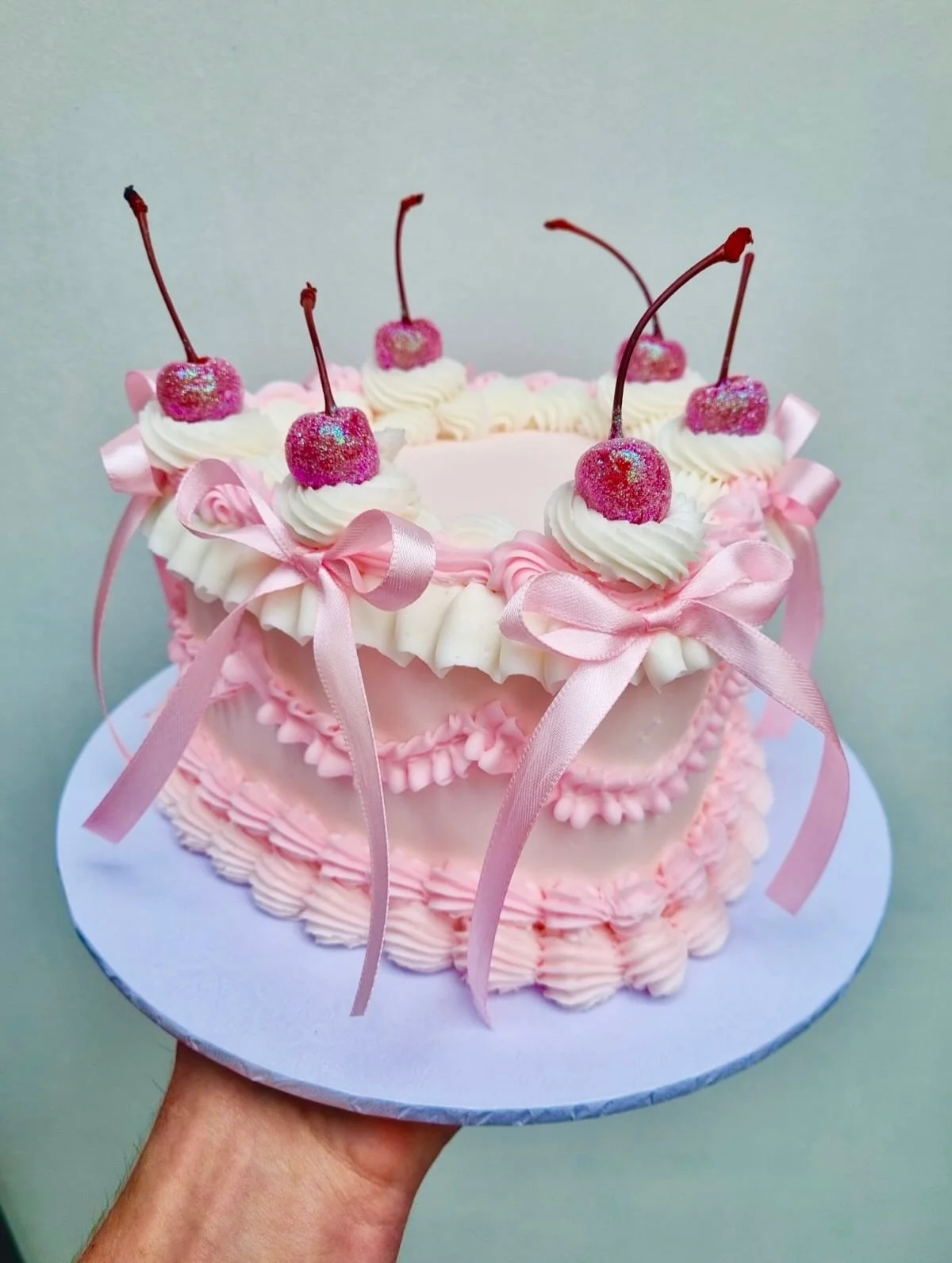 🍒✨ Meet the Cherry Bomb Cutie Cake - now live in our shop &amp; ready to be personalised! 🎀💖
Swipe to see all her pretty angles ➡️

Layers of pink vintage piping, glitter cherries, silky bows and the sweetest retro vibes.
Customise the top with an