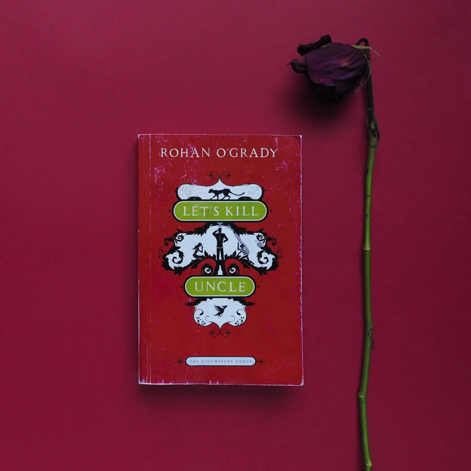 The cover of Let’s Kill Uncle by Rohan O’Grady is red with a small silhoutte of a Canadian mountie, two children, and a cougar in the centre.