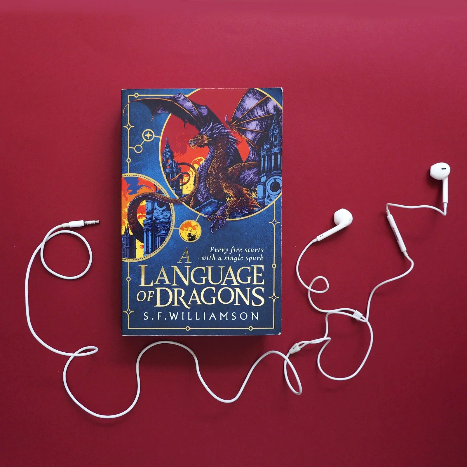 A paperback book on a red background partially encircled by a pair of white headphones.