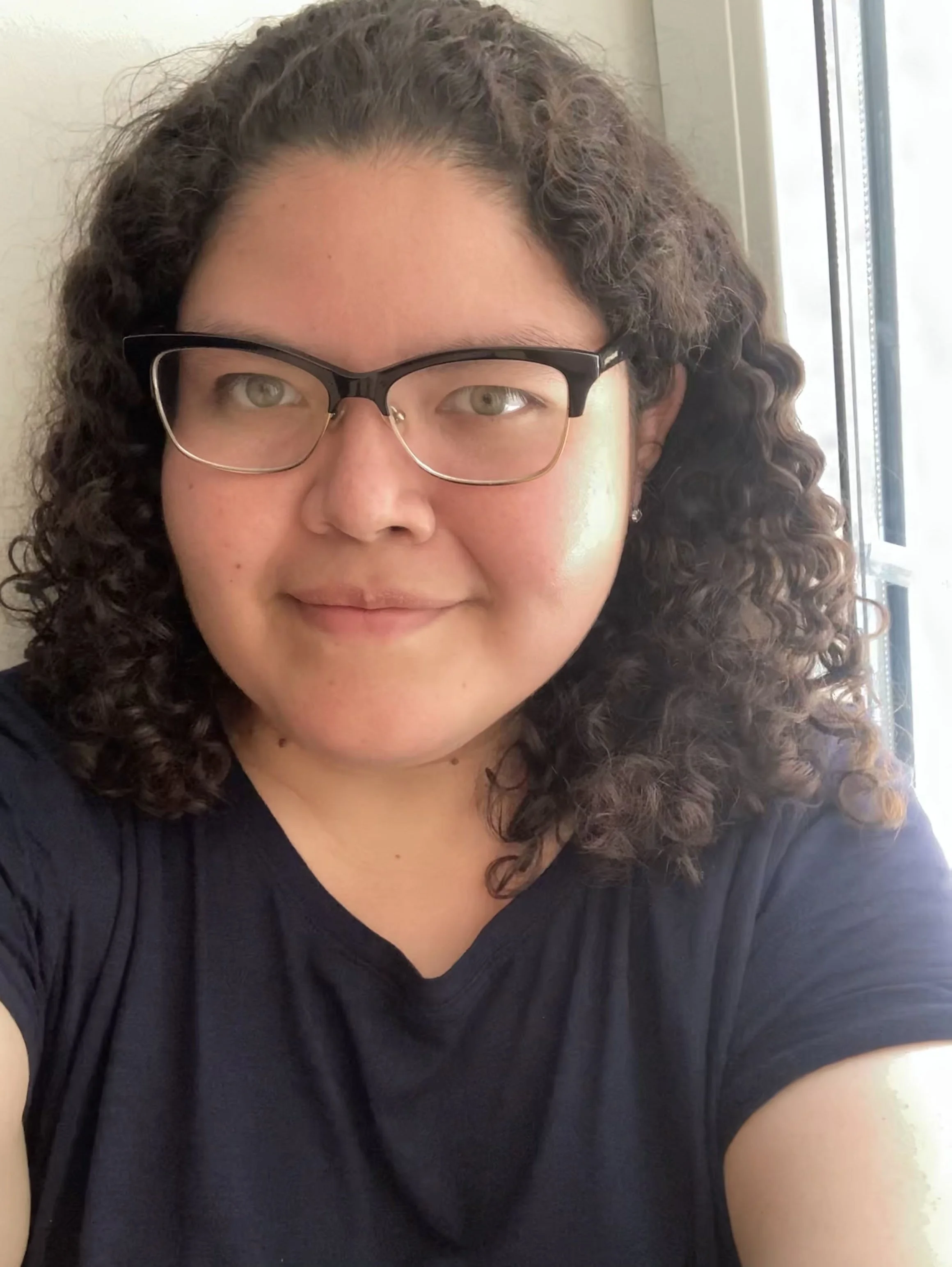 A portrait of Tatiana López, a young woman with shoulder-length curly hair and glasses.