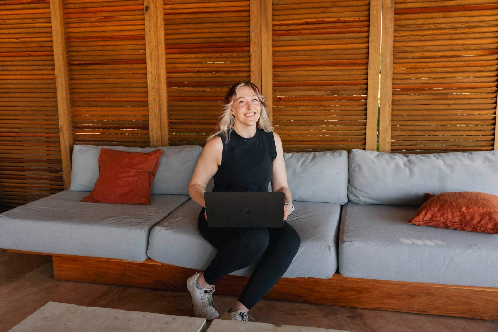 Coach Whitney sitting with laptop on outdoor .sofa in modern wooden lounge