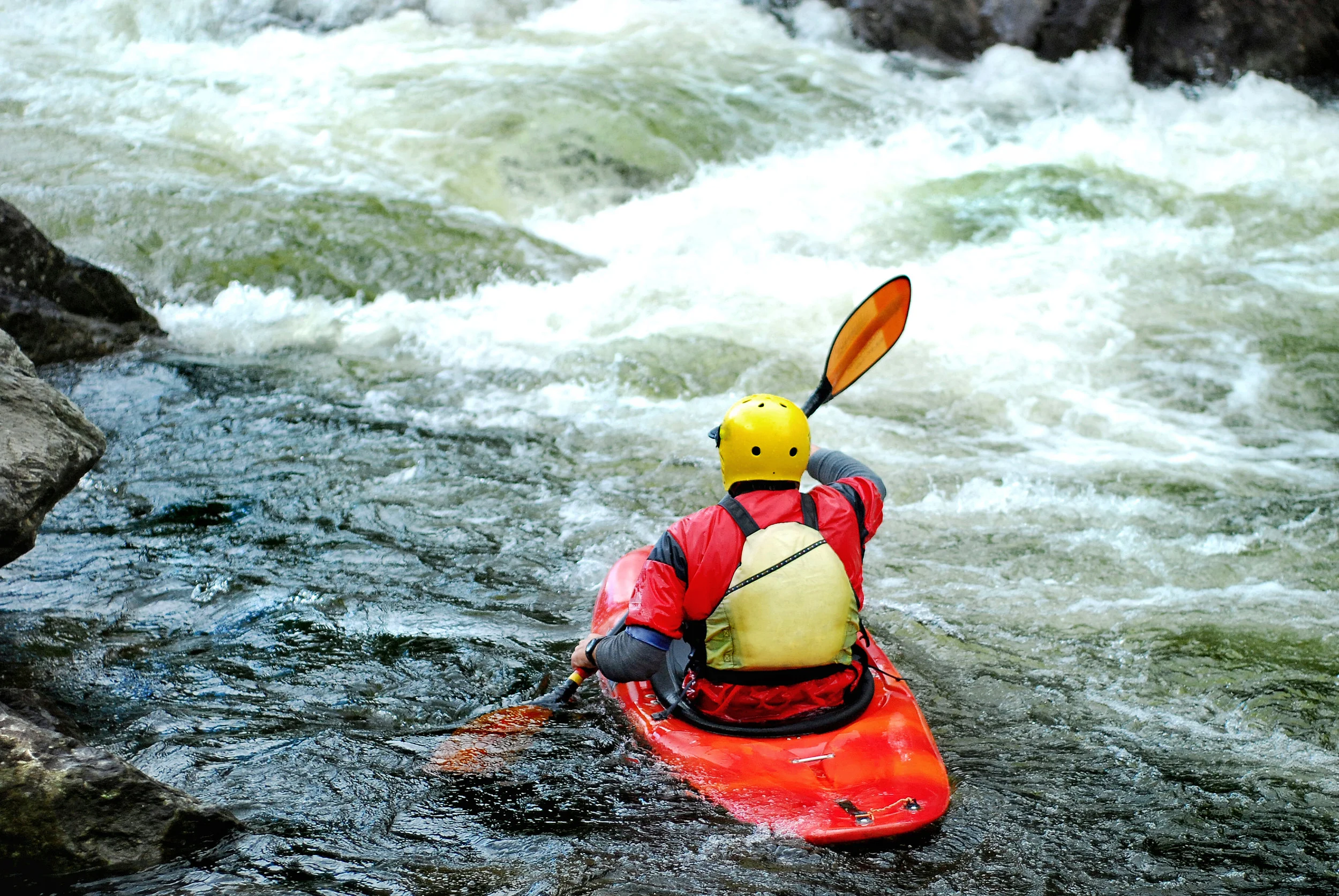 Back view of a red kayaker riding down some whitewater rapids.