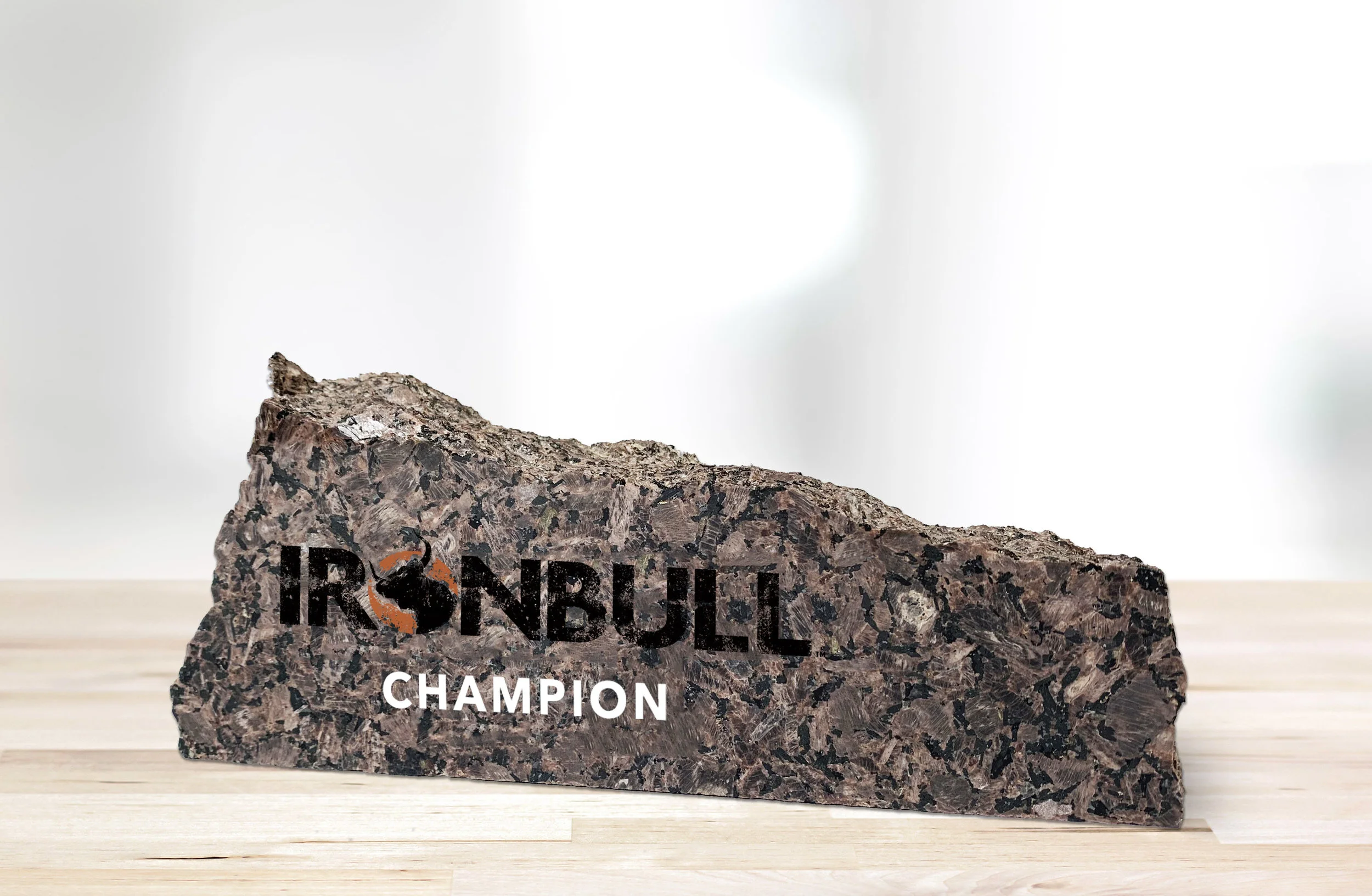 The IRONBULL™ Ring Trophy, a chiseled piece of red granite displaying the IRONBULL™ logo and the word “Champion,” sits on a wooden table.