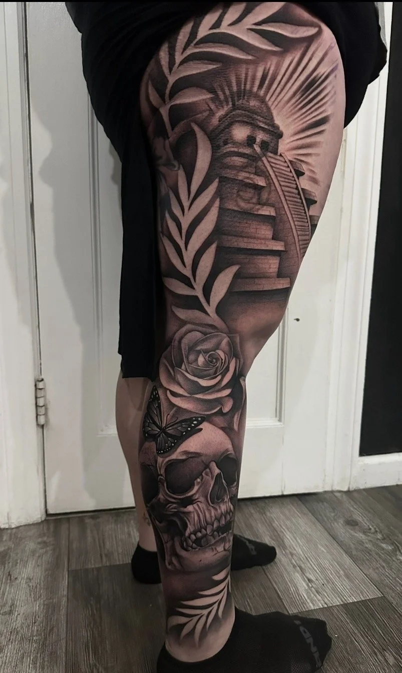 A tattoo sleeve on a person's leg featuring a lighthouse, a rose, a skull, a butterfly, and decorative leaves.