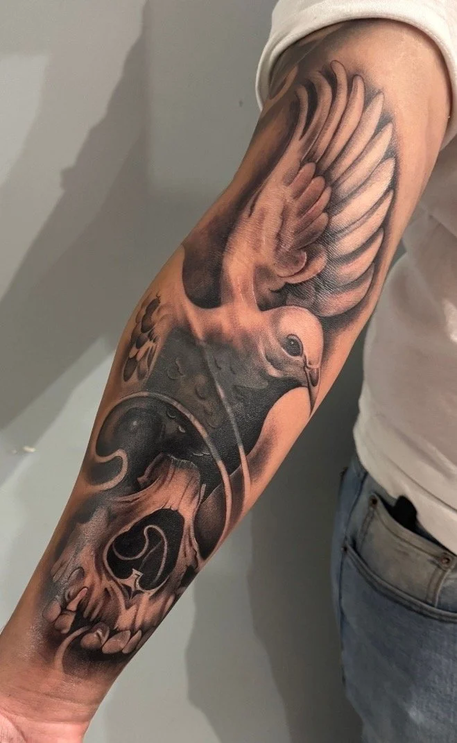 Tattoo of a bird flying out of a skull on a person's forearm.