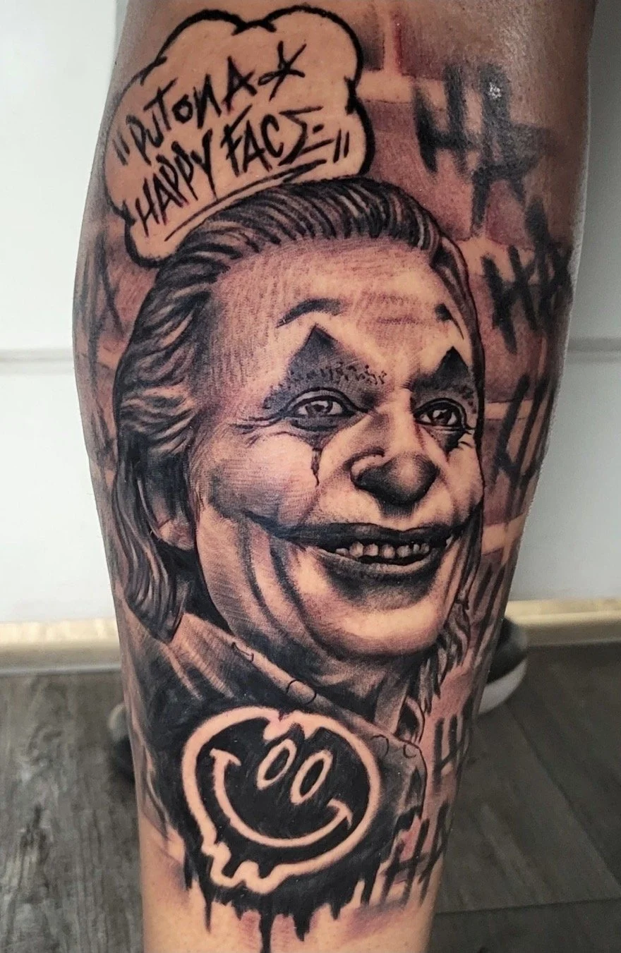 Tattoo of a smiling clown with exaggerated features, including a painted face, with words above and below. The words above the clown's head say, "AUTOMATX HAPPY FACE" inside a speech bubble. The words below the clown are "COC." The tattoo is detailed