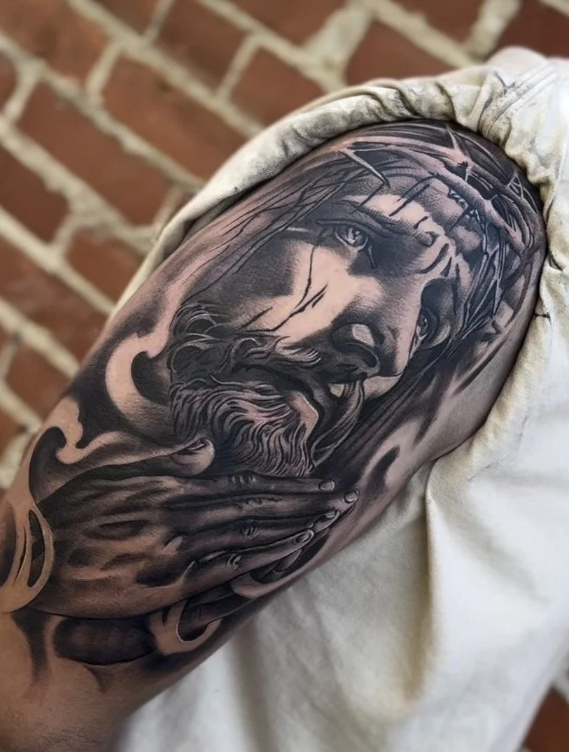 Black and gray tattoo of Jesus Christ wearing a crown of thorns, with a hand resting on his face, on a person's upper arm.
