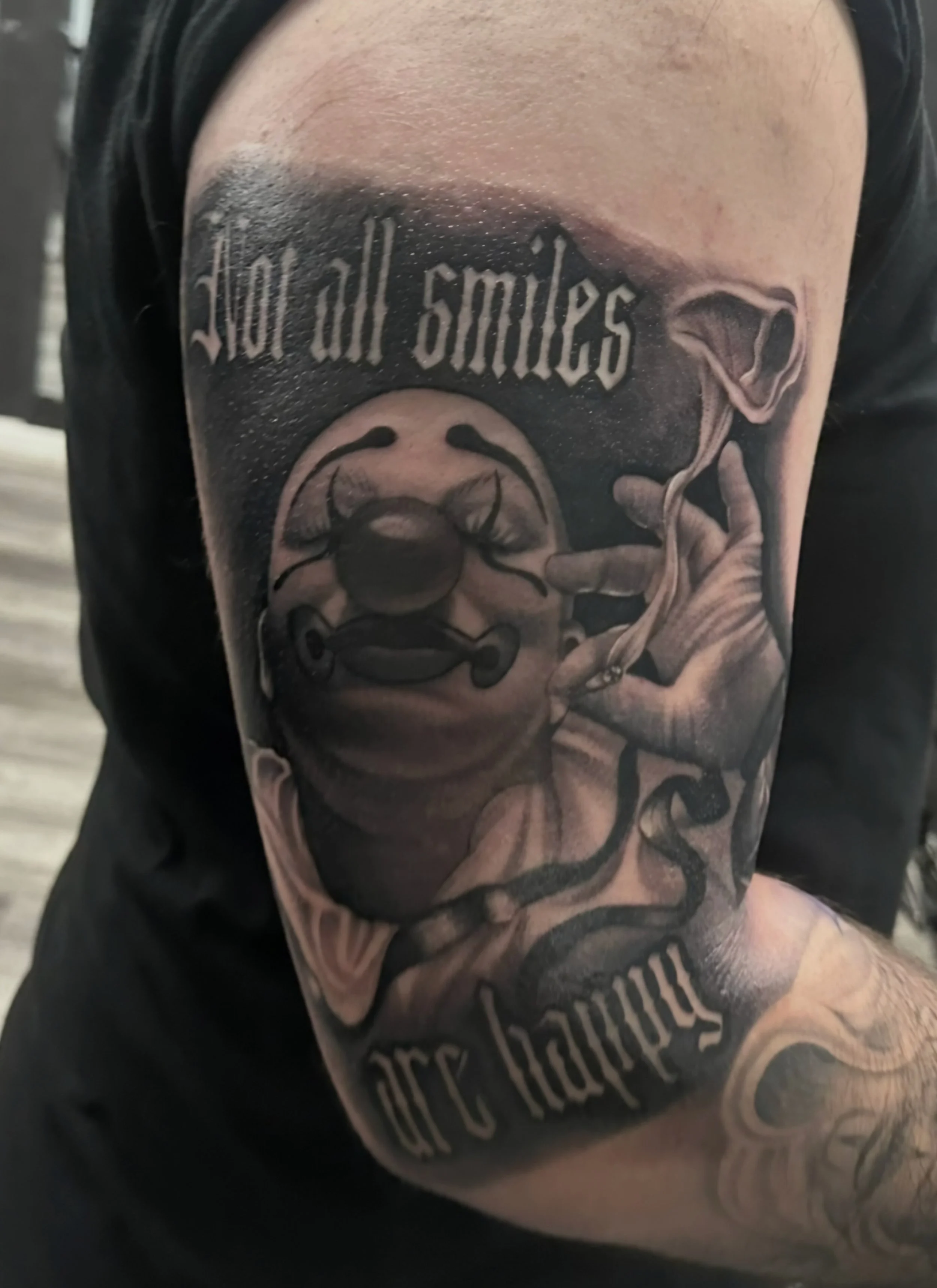 Close-up of a tattoo on a person's upper arm featuring text and a design of a woman with slicked-back hair, large earrings, and a confident expression, with additional text around her.