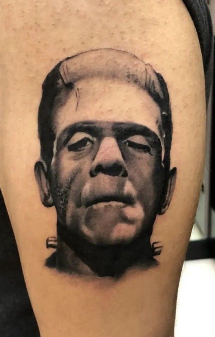 Black and gray tattoo of a man's face on a person's upper arm, with a serious expression.