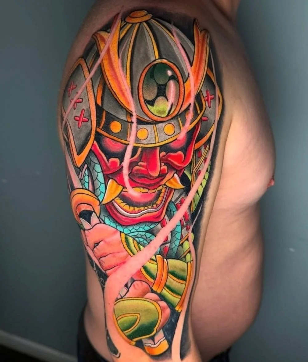 Colorful Japanese-style tattoo featuring a fierce warrior with a smiling face wearing a helmet with an eye on it, holding a sword with green and yellow details.