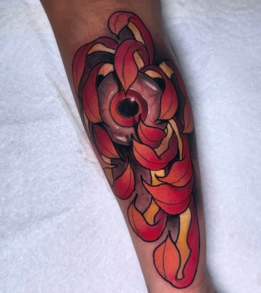 A colorful tattoo of a red eye surrounded by stylized red and orange flames on a person's arm.
