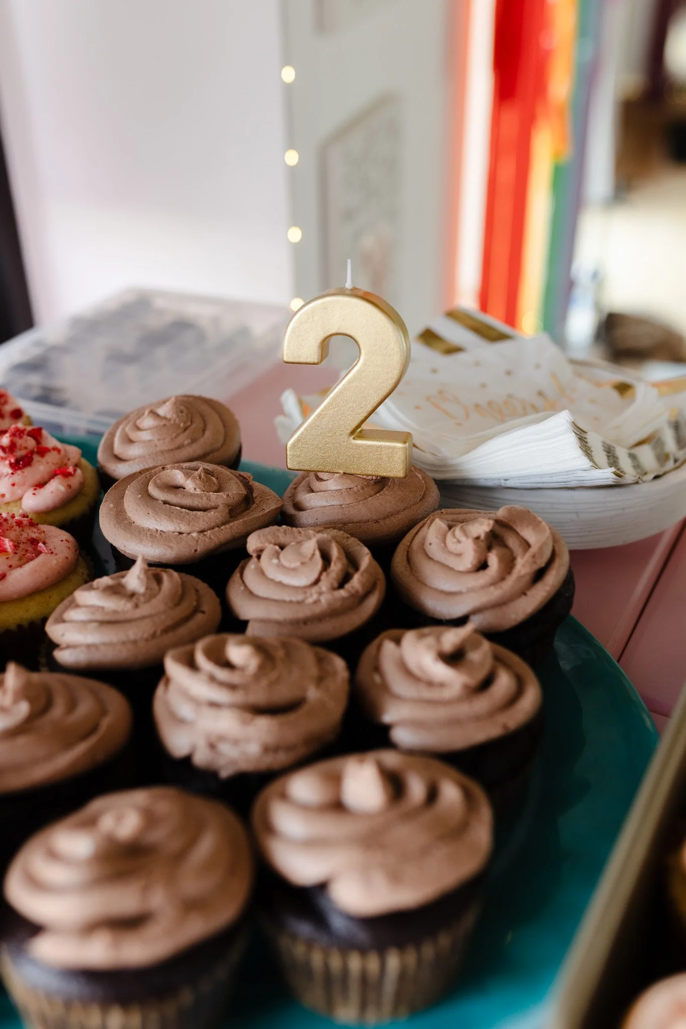 Cupcakes with chocolate frosting arranged on a tray, topped with a gold number 2 candle, indicating a celebration.