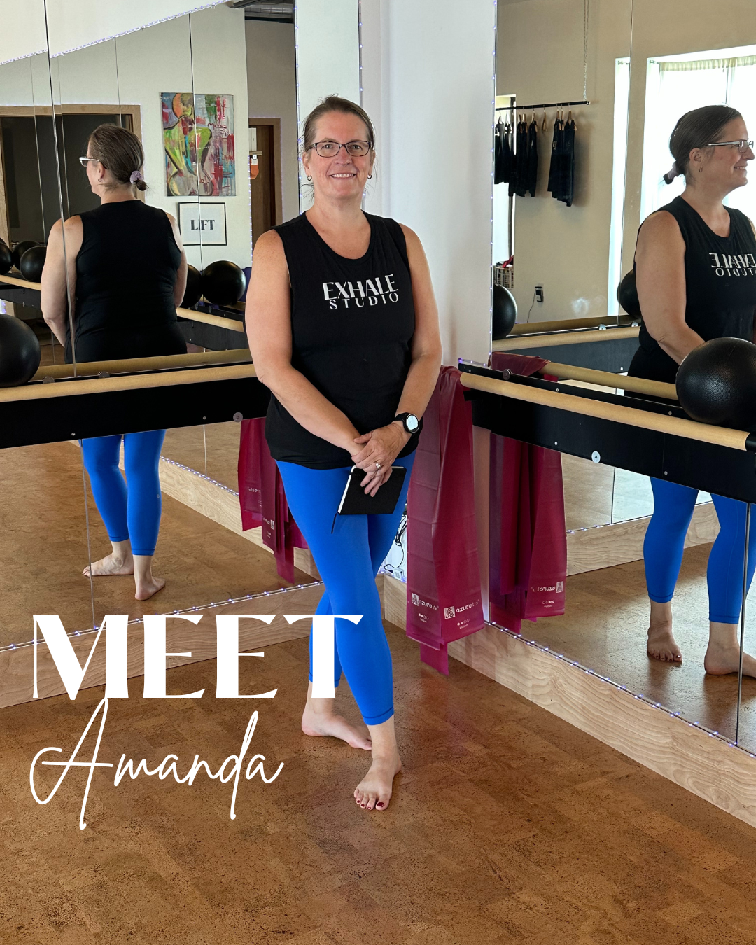 A woman standing in a dance studio with mirrored walls, wearing a black sleeveless shirt with 'EXHALE STUDIO' printed on it and blue leggings. She is smiling and holding a phone, with her reflection visible in the mirrors. The studio has a ballet barre, black exercise balls, artwork on the wall, and other exercise mats visible in the background. The text overlay says 'MEET Amanda.'