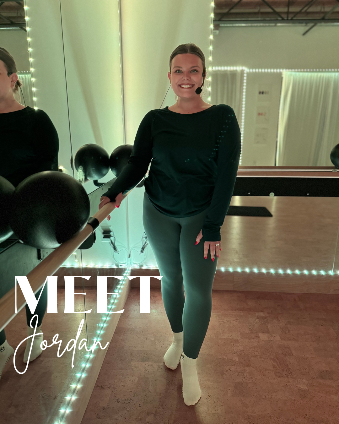 A woman smiling in a fitness studio with a mirror and wall decorated with string lights, wearing a black long sleeve top, gray leggings, and white socks, holding a wooden ballet barre, with the caption "Meet Jordan" overlaying the image.