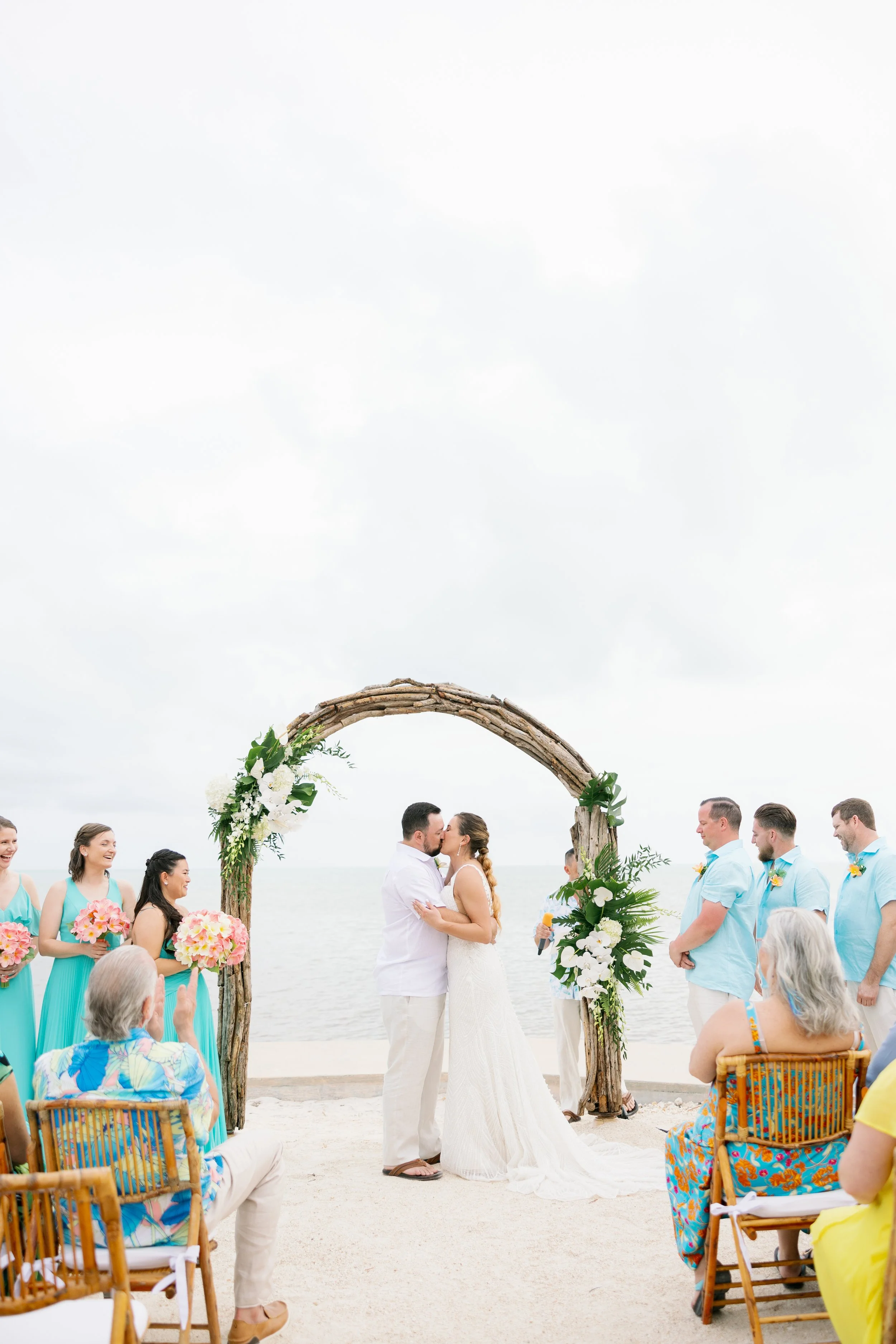 A wedding ceremony at The Oasis Islamorada couple kissing under a wooden arch decorated with flowers.