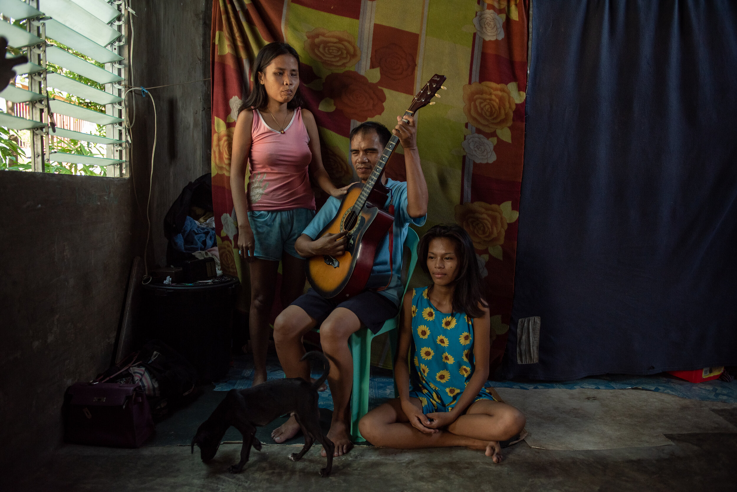 Typhoon Haiyan survivors Wenife Bacunata (left) and daughter Angelica Bacunata (right) sings while her father Joseph Bacunata (middle) plays the guitar. Before they were resettled, the blind couple earned their living by playing music at a local rad