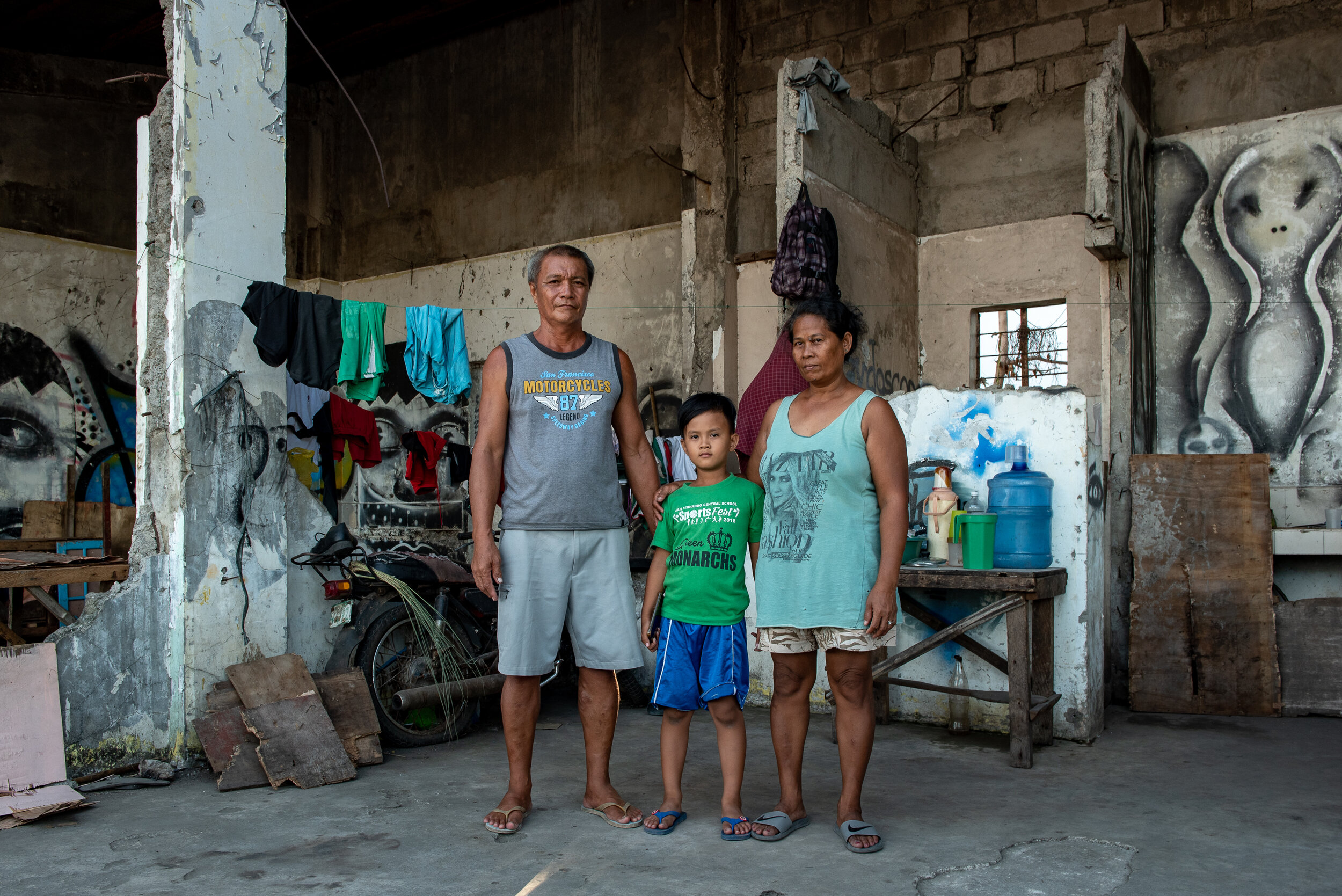  53 year old fisherman Gerry Diablo (left) along with his son EJ (center) and Risa (right) are one of the families that sought shelter in this empty graffiti-clad space along the coastal area of Real Street, Tacloban City. 