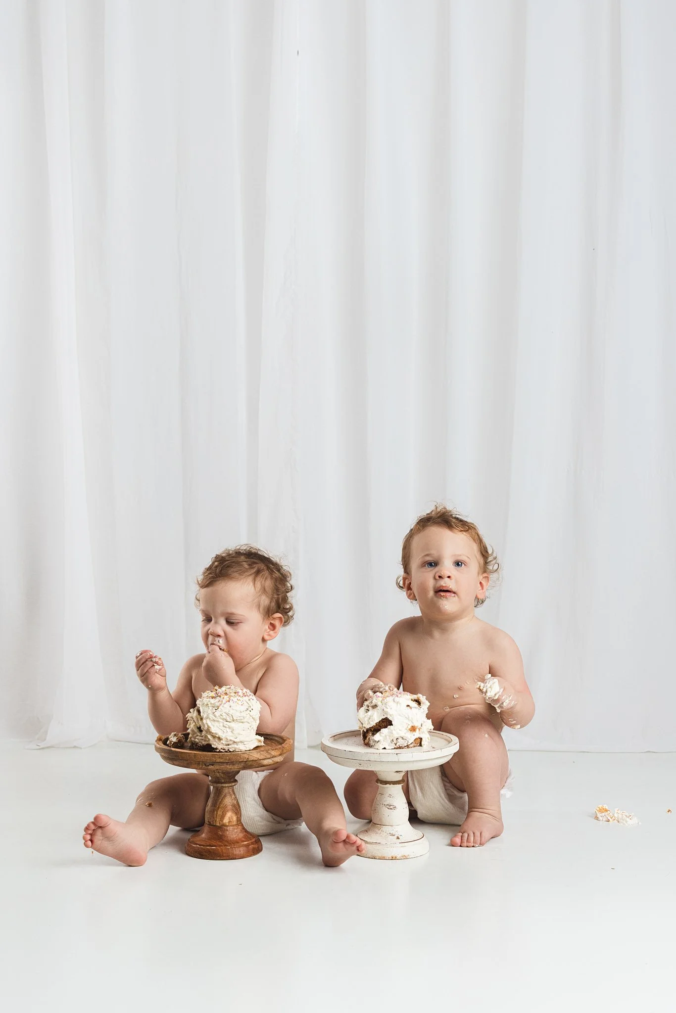 Baby crawling away during a cake smash session while another explores cake on a stand in Seattle studio