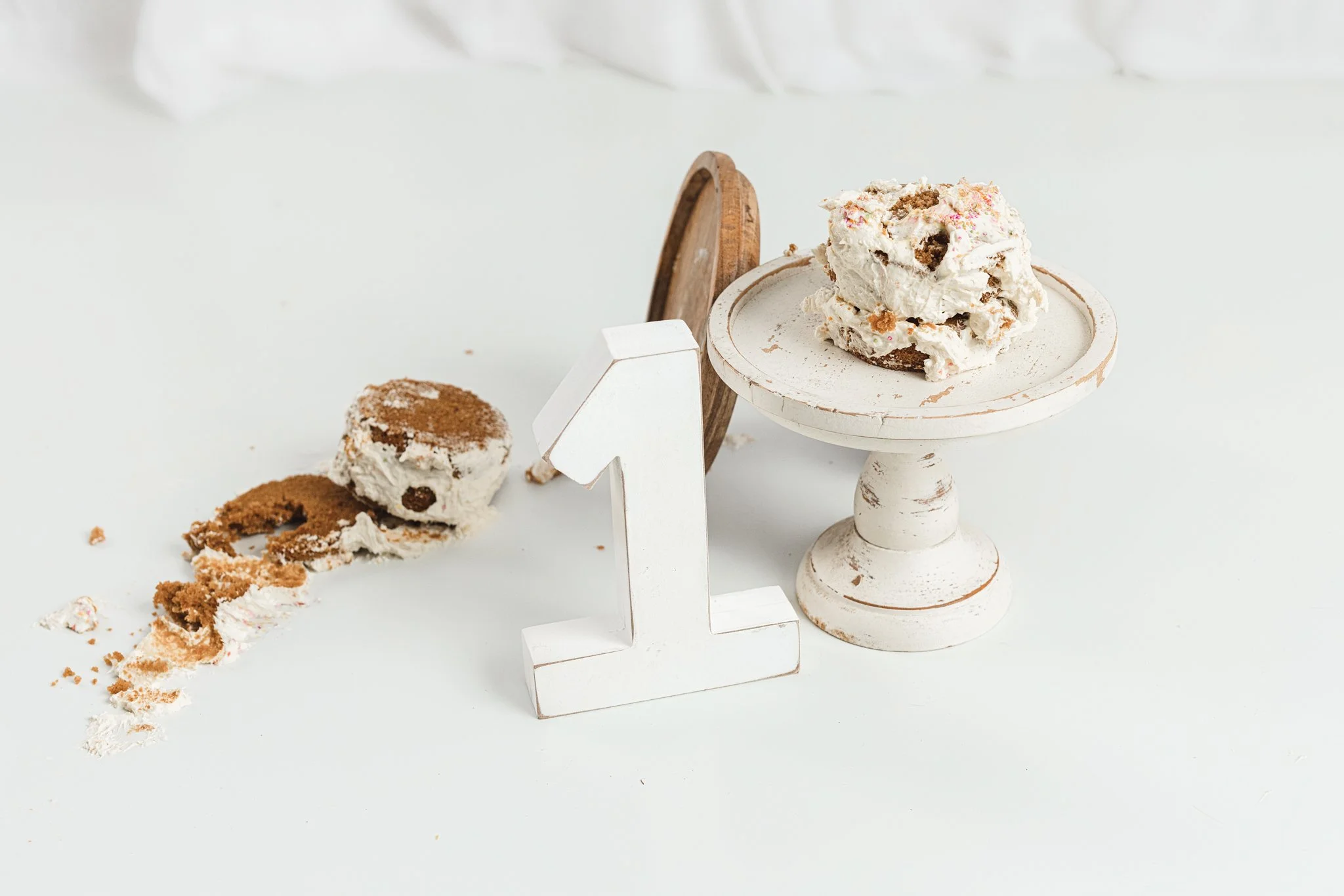 First birthday cake smash detail showing a messy cake on a pedestal with a wooden number one, capturing the aftermath of a baby-led milestone session in a studio