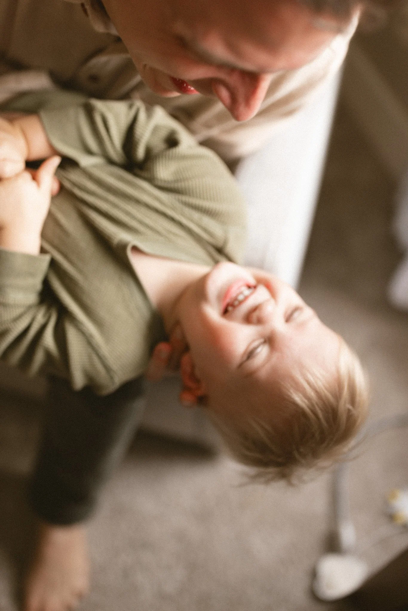 A toddler laughs while being playfully held upside down by a parent during a cozy in-home lifestyle family photography session in Seattle.