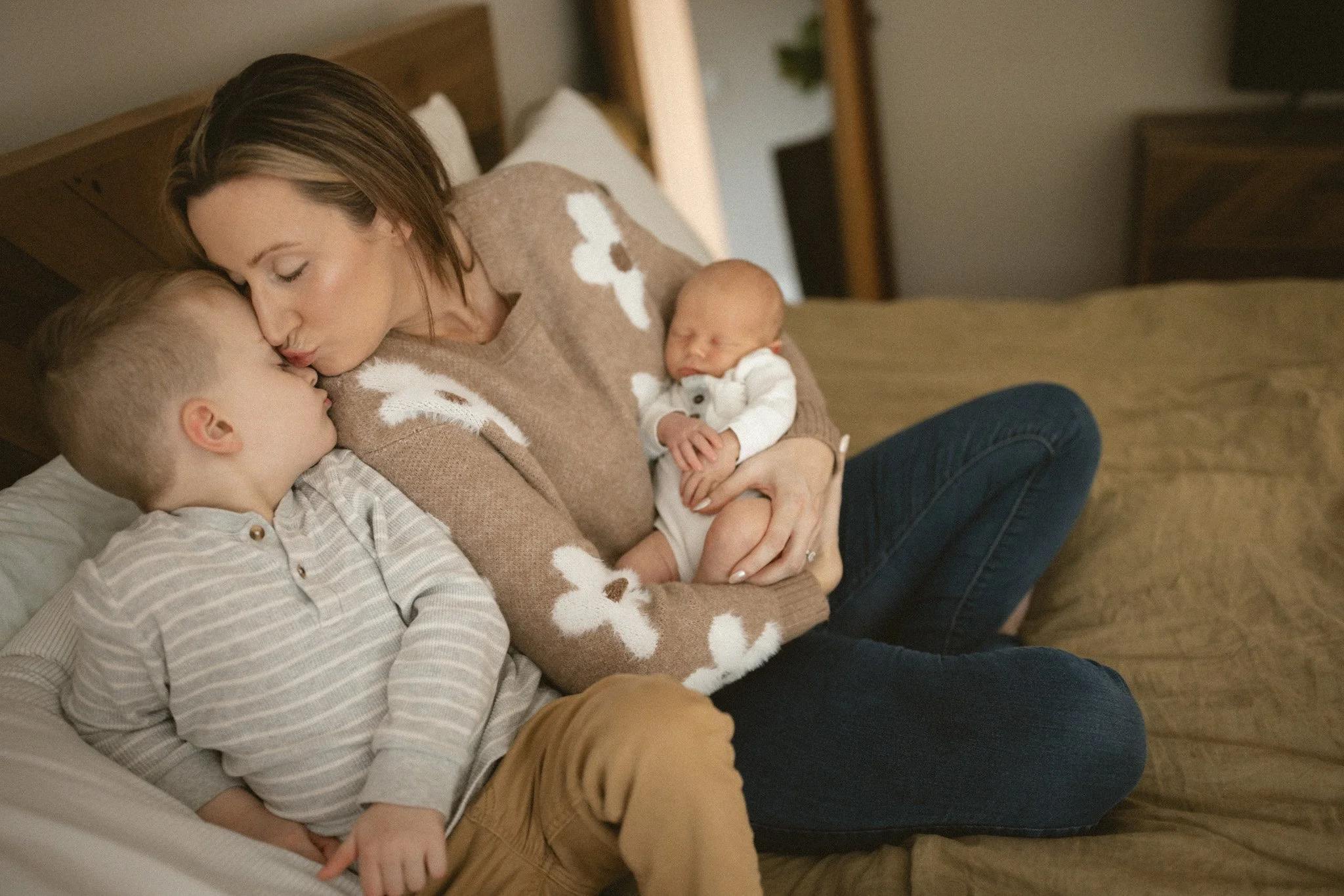 A mother kisses her toddler while holding her newborn during a calm in-home newborn family photography session in the Bellevue and Redmond area.