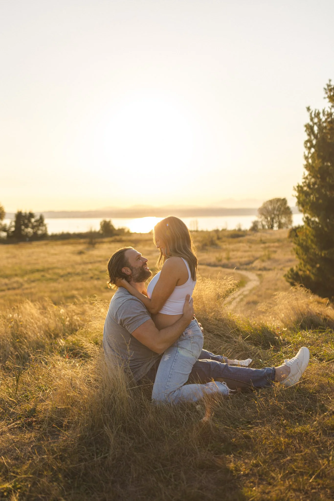 Expecting couple sharing a quiet, intimate moment in a golden field at sunset during an outdoor maternity photography session.