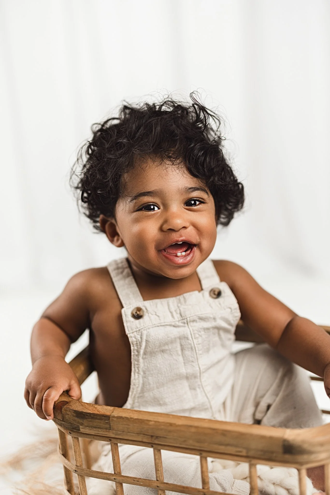 Smiling baby sitting in a wooden basket during a studio milestone photography session with a bright, minimal background.