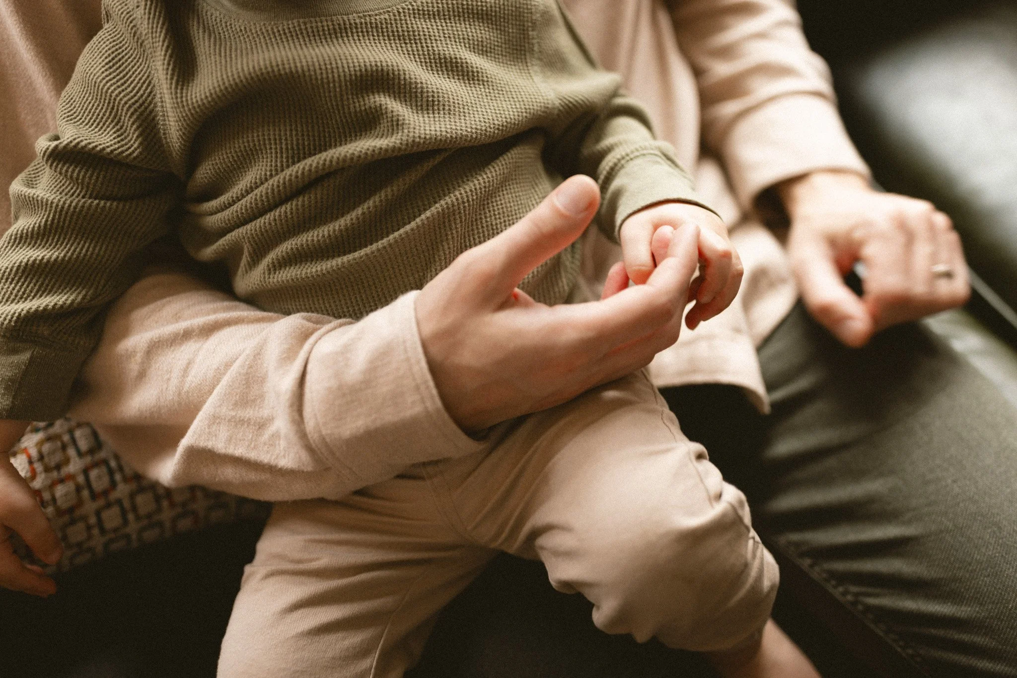 A father gently holds his toddler’s hand during a cozy in-home family photography session in Seattle.