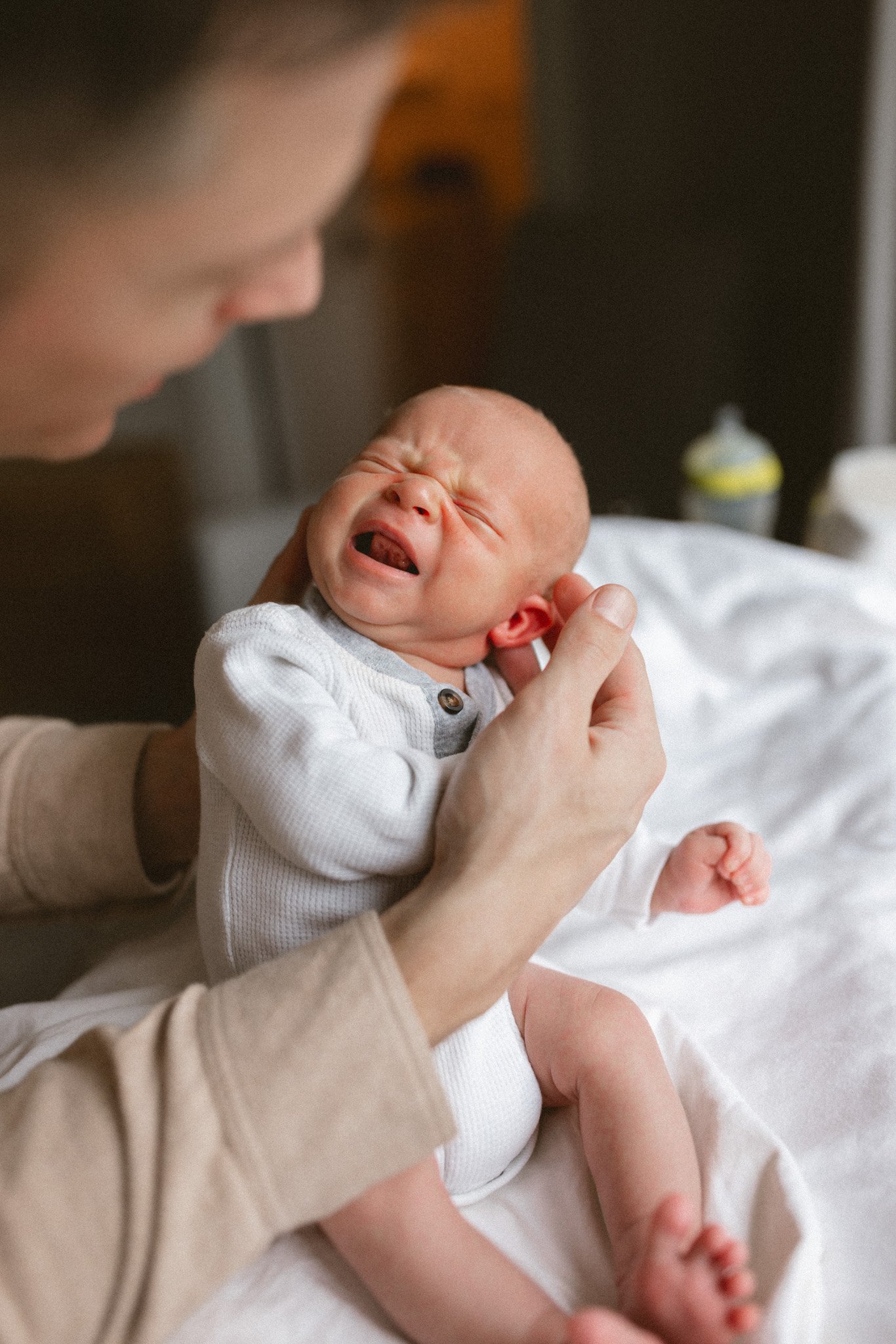 A newborn cries softly while being comforted in their father’s arms during a cozy in-home newborn photography session in Seattle.