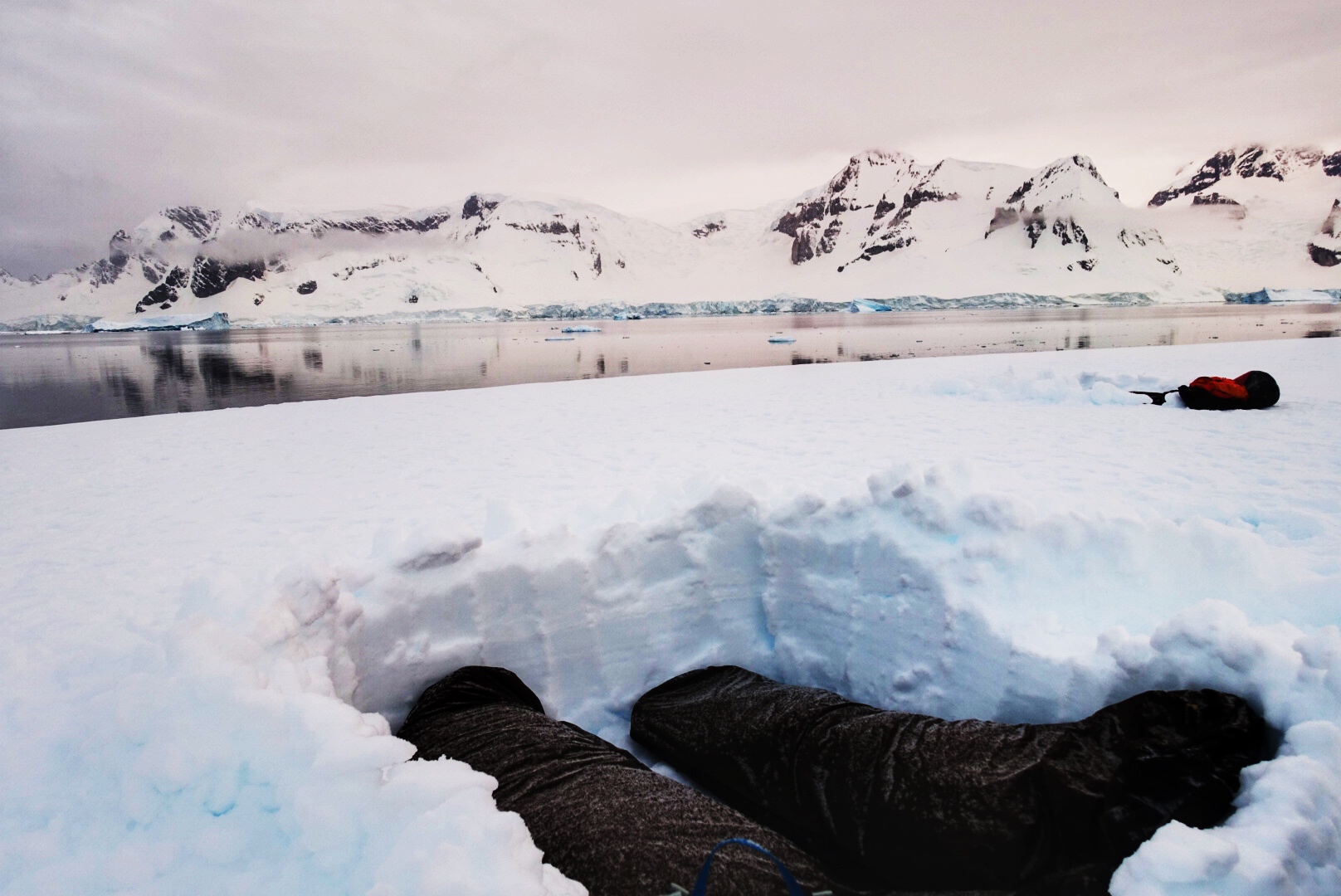 Camping in Antarctica: 2 sleeping bags in a snow hole with snow-covered mountains in the background