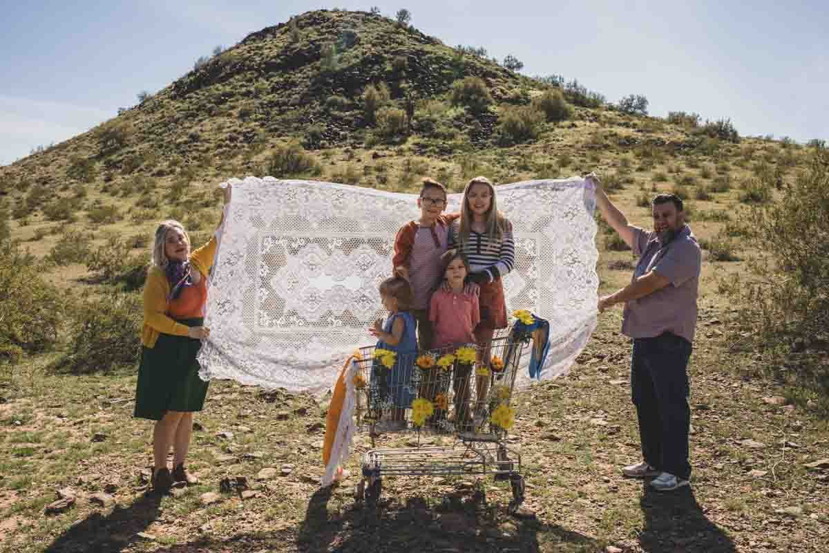  Family posing together in a shopping cart with lace tablecloth backdrop during Creative Photography Family Session with best Phoenix family photographer, Jennifer Lind Schutsky. 