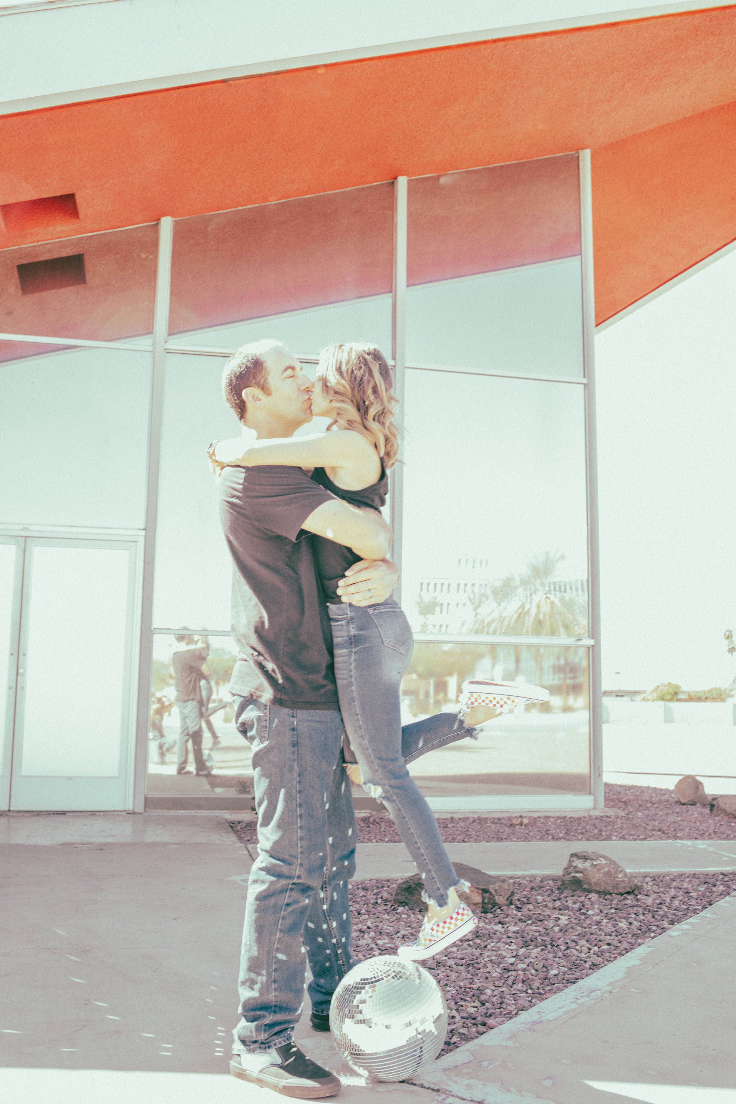 Couple poses for their retro bike and skateboard photoshoot with a disco ball at Bowlero in Phoenix, Arizona by the most creative family photographer in Phoenix; Jennifer Lind Schutsky.