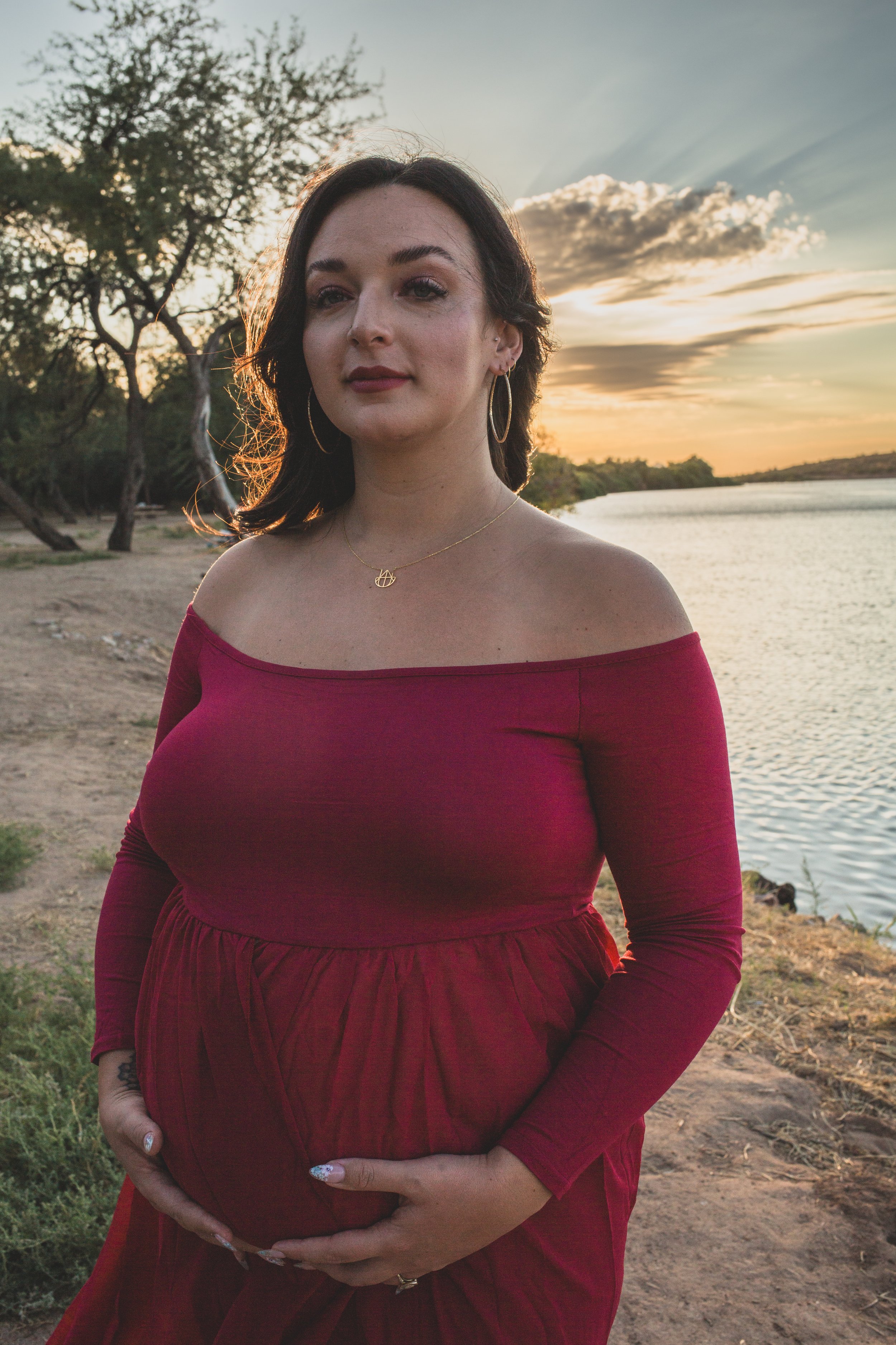 Pregnant woman in a red dress at Sunset for maternity photos in front of the Salt River by Phoenix maternity photographer in Arizona; Jennifer Lind Schutsky.