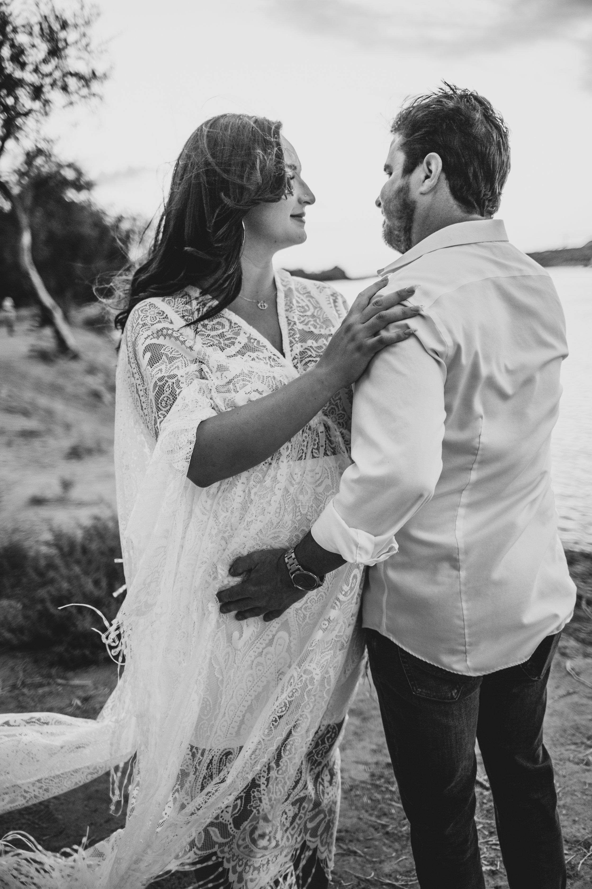 Romantic couple poses with the wind in their hair for maternity photos near the water at the Salt River by timeless Phoenix maternity photographer; Jennifer Lind Schutsky.