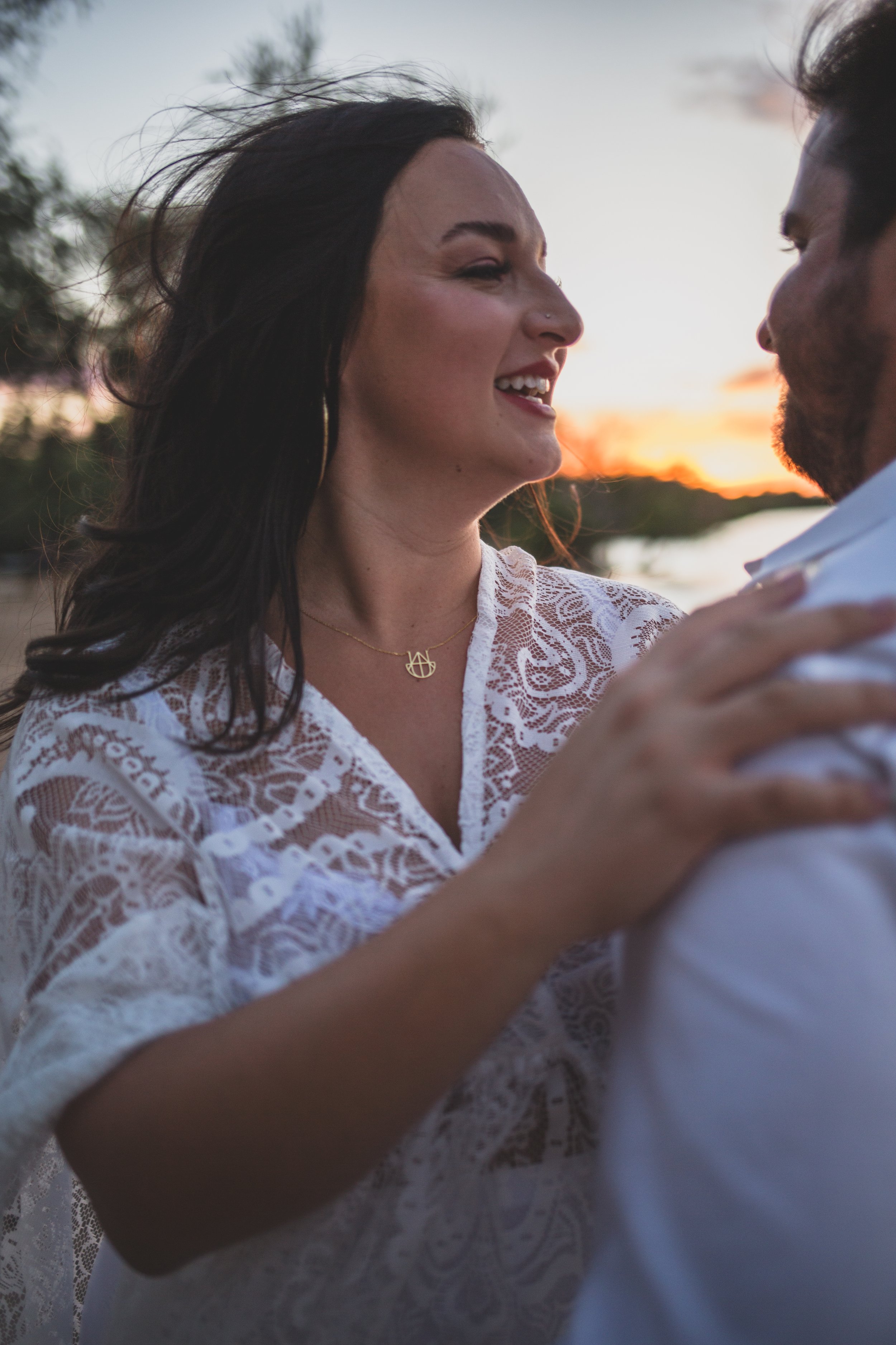 Romantic couple poses with the wind in their hair for maternity photos near the water at sunset the Salt River by timeless Phoenix maternity photographer; Jennifer Lind Schutsky.