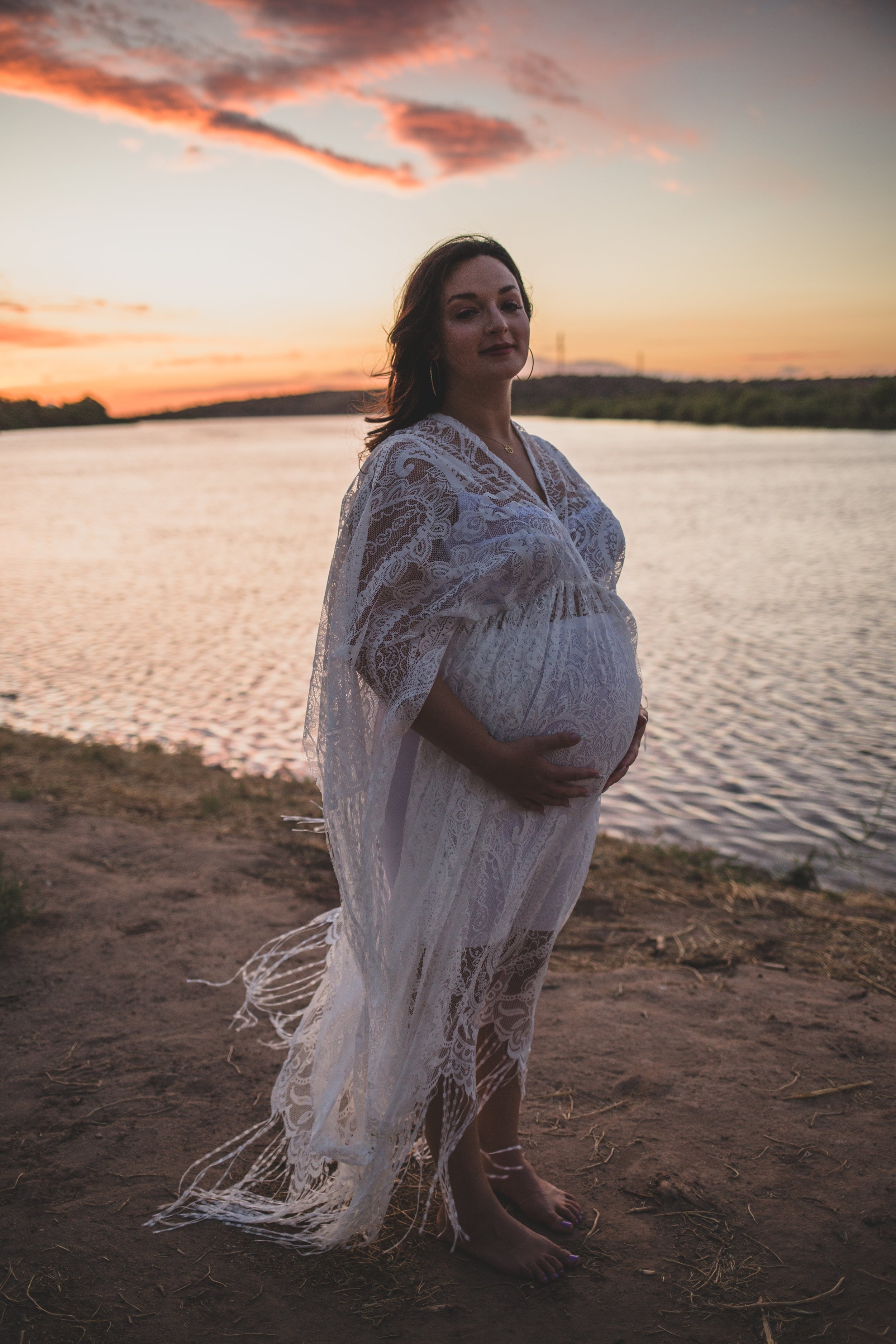Romantic pregnant mother poses with the wind in their hair for maternity photos near the water at sunset the Salt River by timeless Phoenix maternity photographer; Jennifer Lind Schutsky.