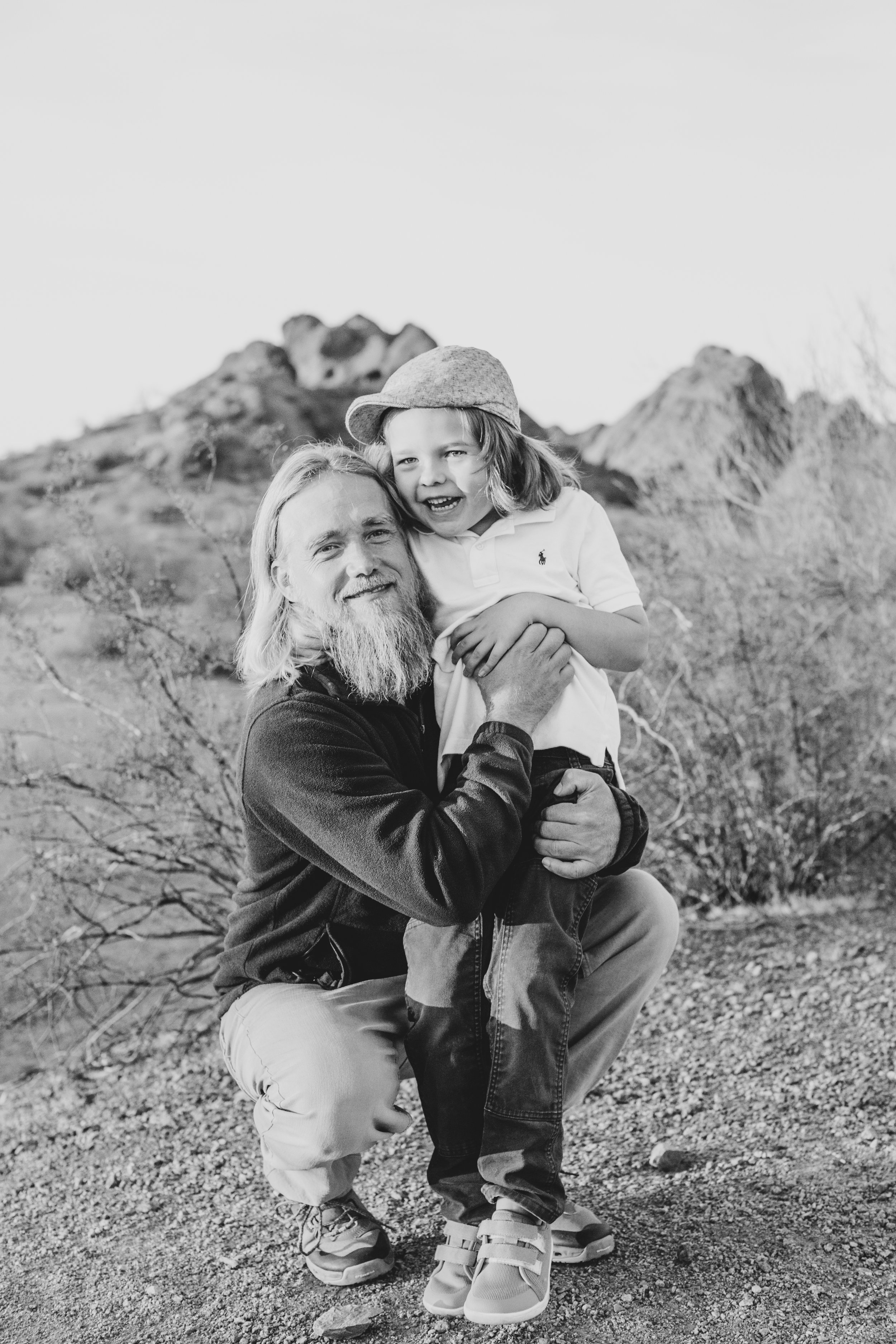 Casual dressed father and son pose together during family desert photo session near Papago Park in Tempe, Arizona by Phoenix based family photographer Jennifer Lind Schutsky. 