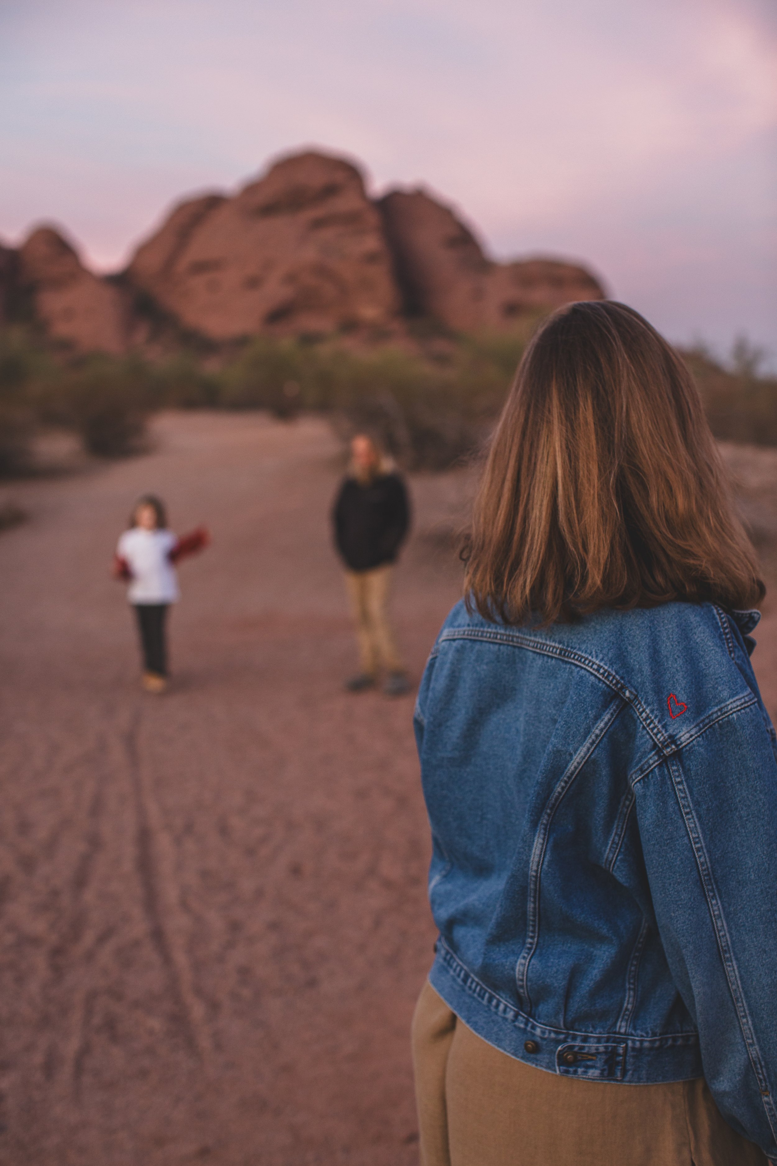 Mom looks over her shoulder at dad and son as they pose for photo by son at family desert photo session near Papago Park in Tempe, Arizona by Phoenix based family photographer Jennifer Lind Schutsky. 