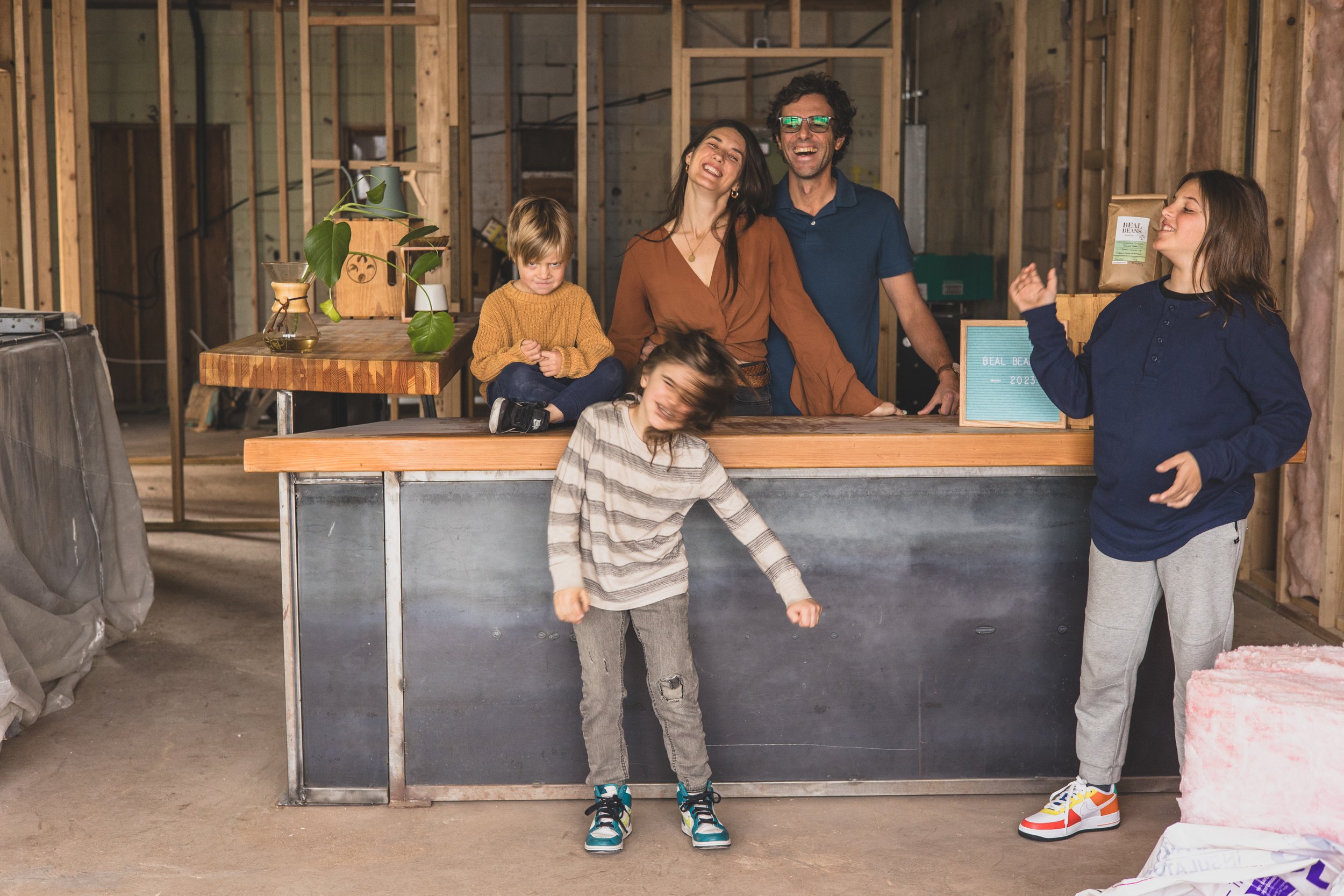 Family poses for their unique photo session behind the countertop in the Beal Beans’ new coffee shop coming to Sunnyslope, AZ by Arizona family photographer, Jennifer Lind Schutsky. 