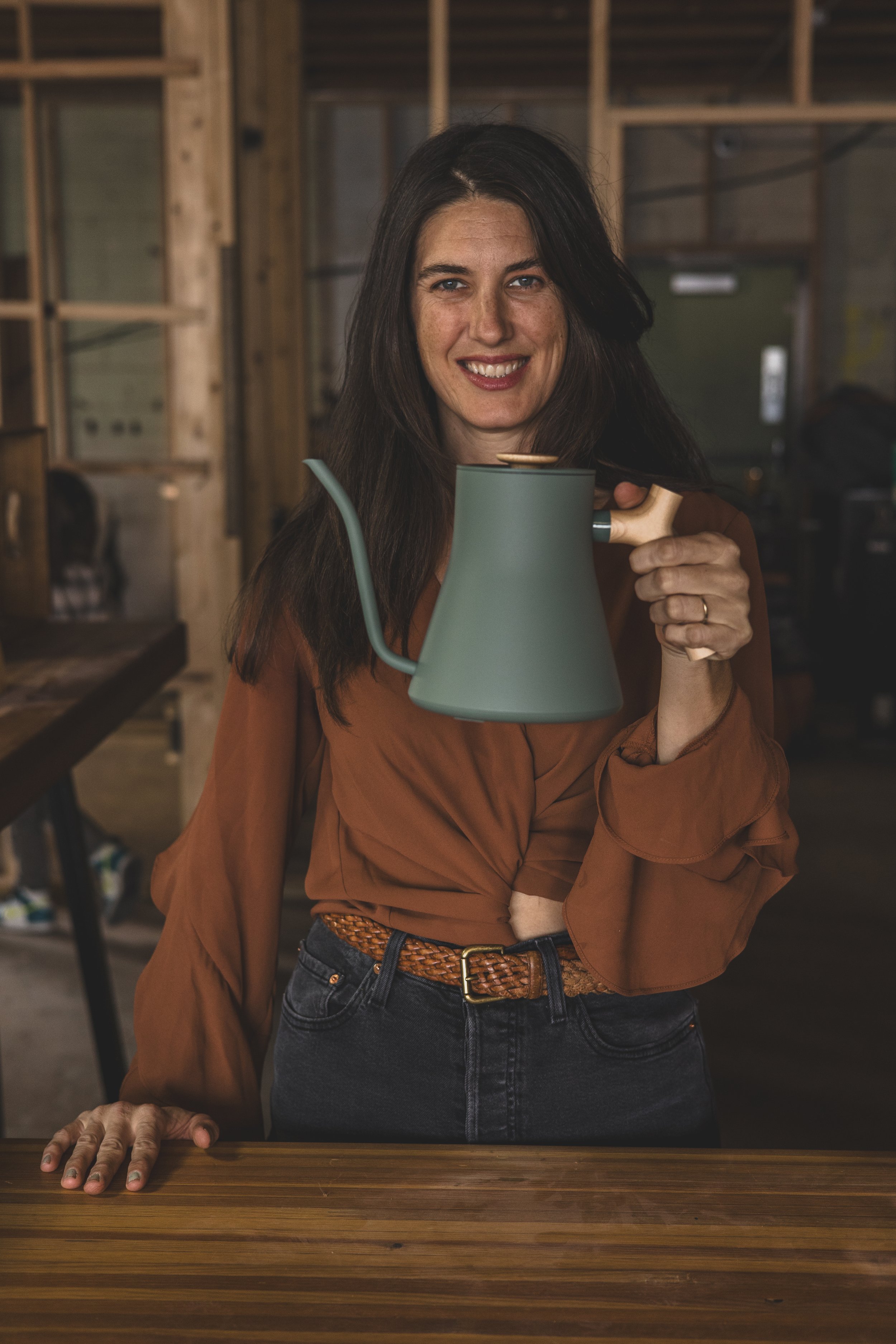 Woman poses with pour over coffee pot in the unfinished Beal Beans’ new coffee shop coming to Sunnyslope, AZ by Arizona family photographer, Jennifer Lind Schutsky. 