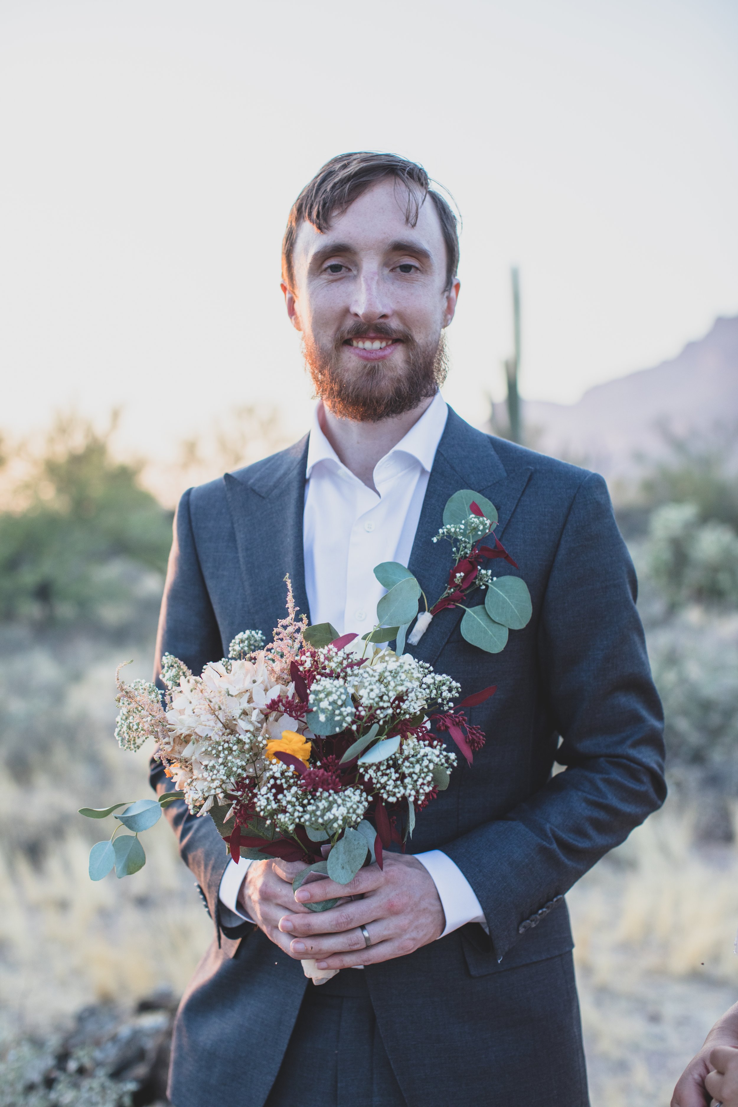 Groom with his bride’s wildflower floral bouquet for their Superstition Mountain intimate wedding near Phoenix, Arizona by wilderness wedding photographer, Jennifer Lind Schutsky. 