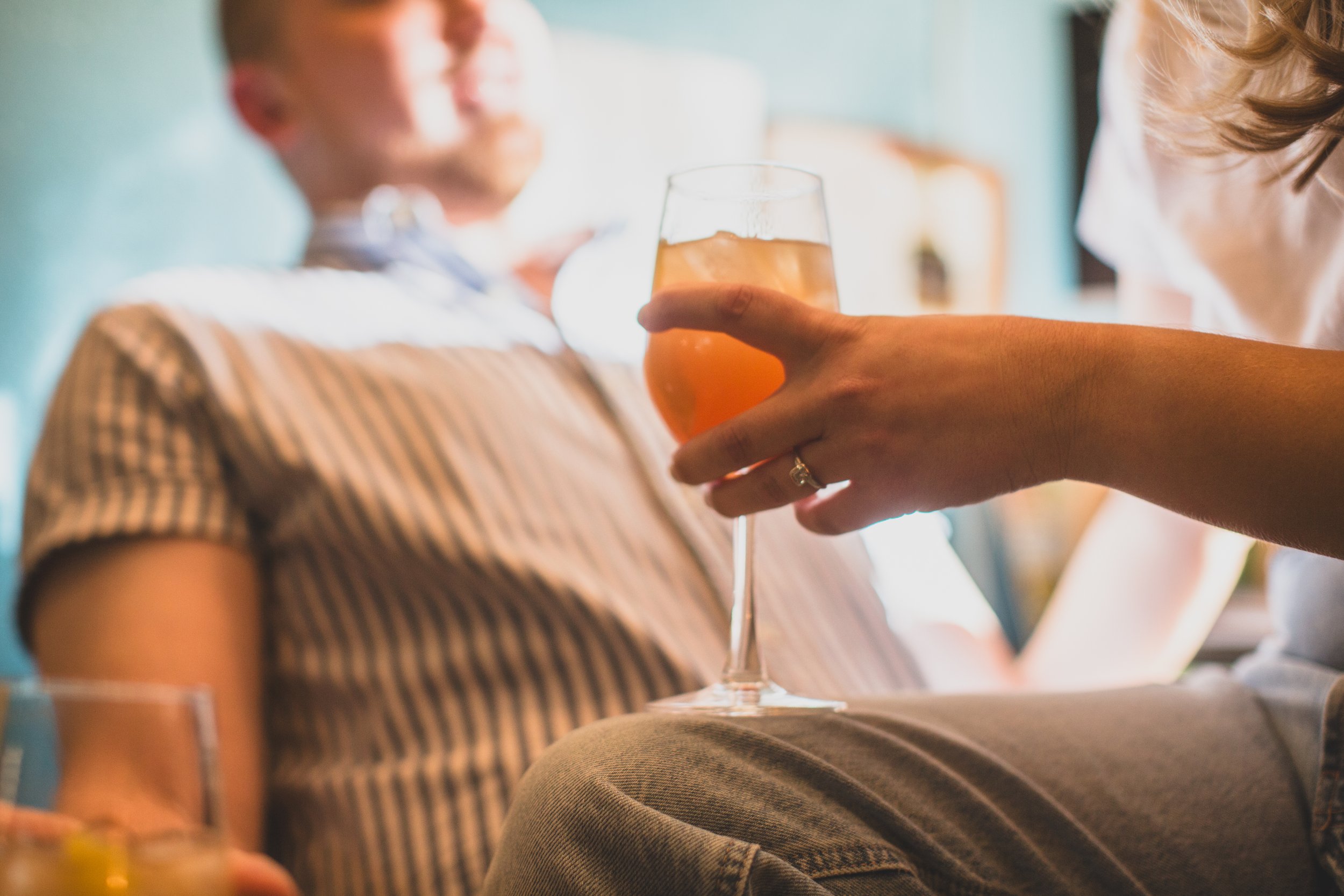 Woman sits on fiances’ lap with drink in hand during their in-home engagement photo session with Phoenix based creative wedding photographer; Jennifer Lind Schutsky. 