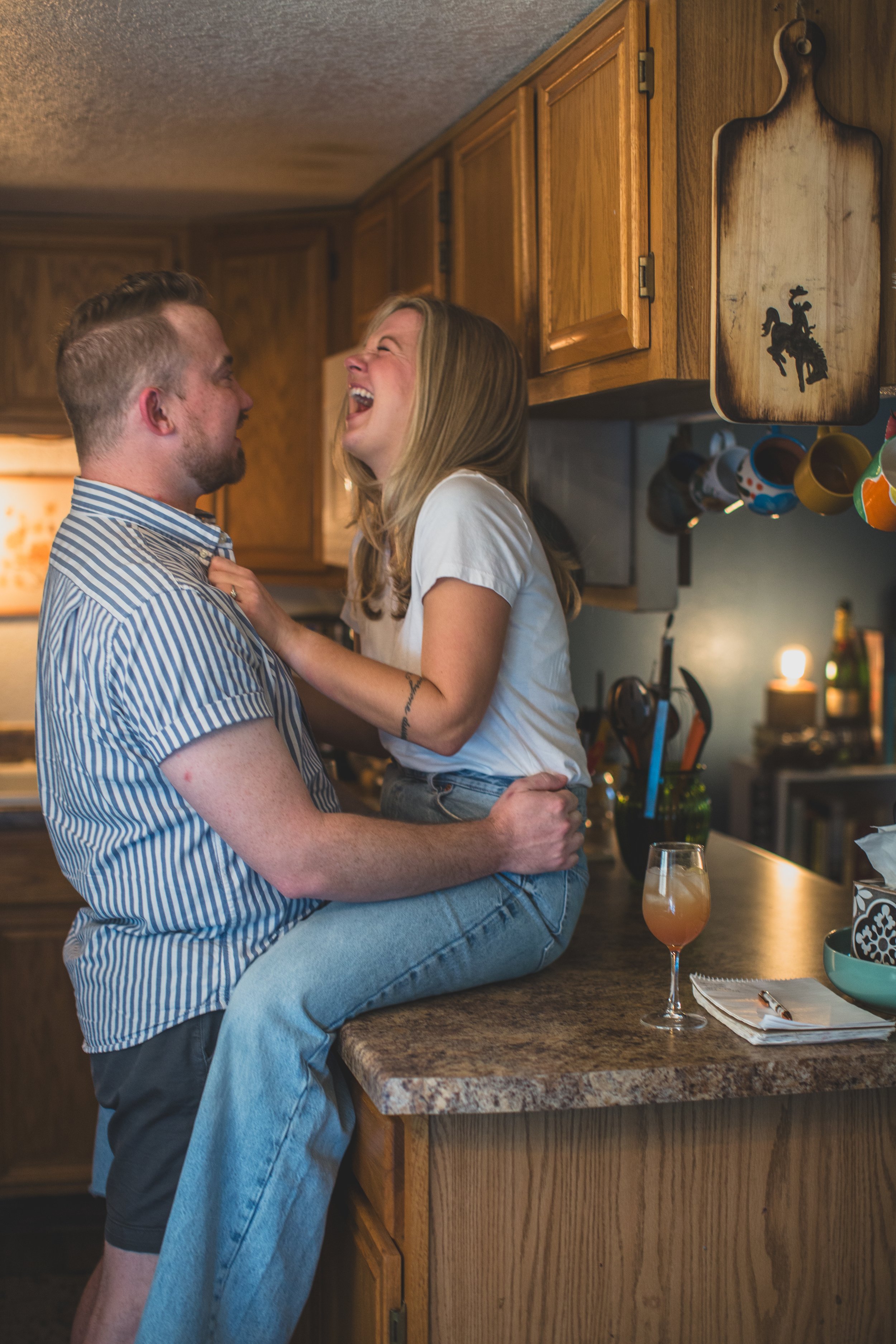 Adorable couple laugh on countertop during their in-home engagement photo session with Phoenix based creative wedding photographer; Jennifer Lind Schutsky. 