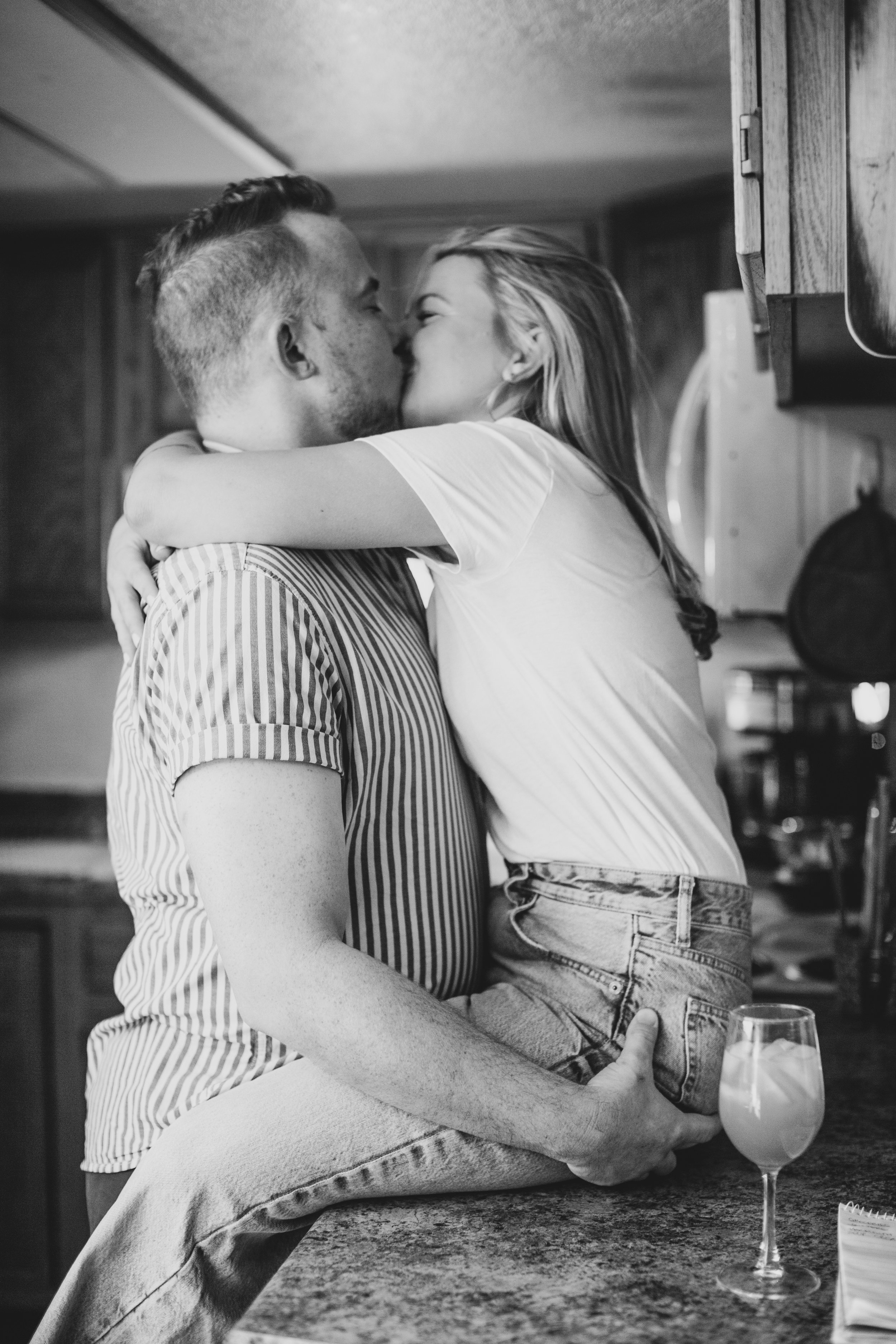 Adorable couple hug and kiss on countertop during their in-home engagement photo session with Phoenix based creative wedding photographer; Jennifer Lind Schutsky. 