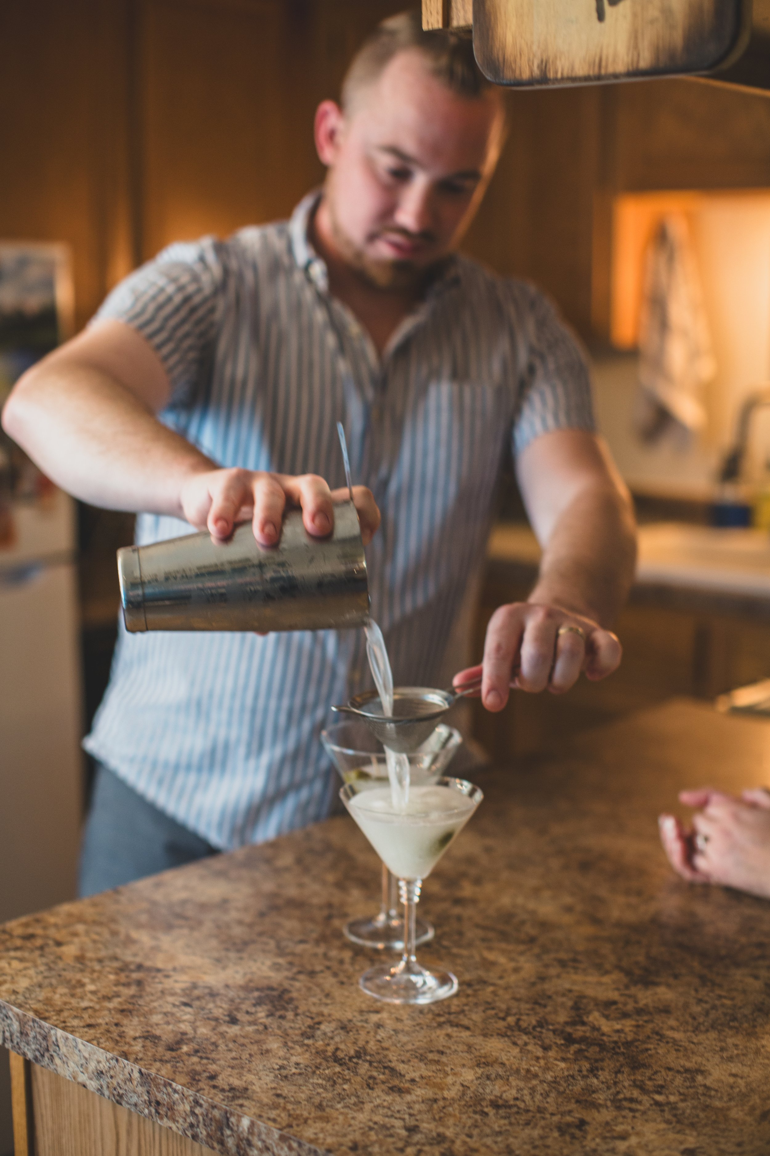 Man makes cocktails for the couple during their in-home engagement photo session with Phoenix based romantic and creative wedding photographer; Jennifer Lind Schutsky. 
