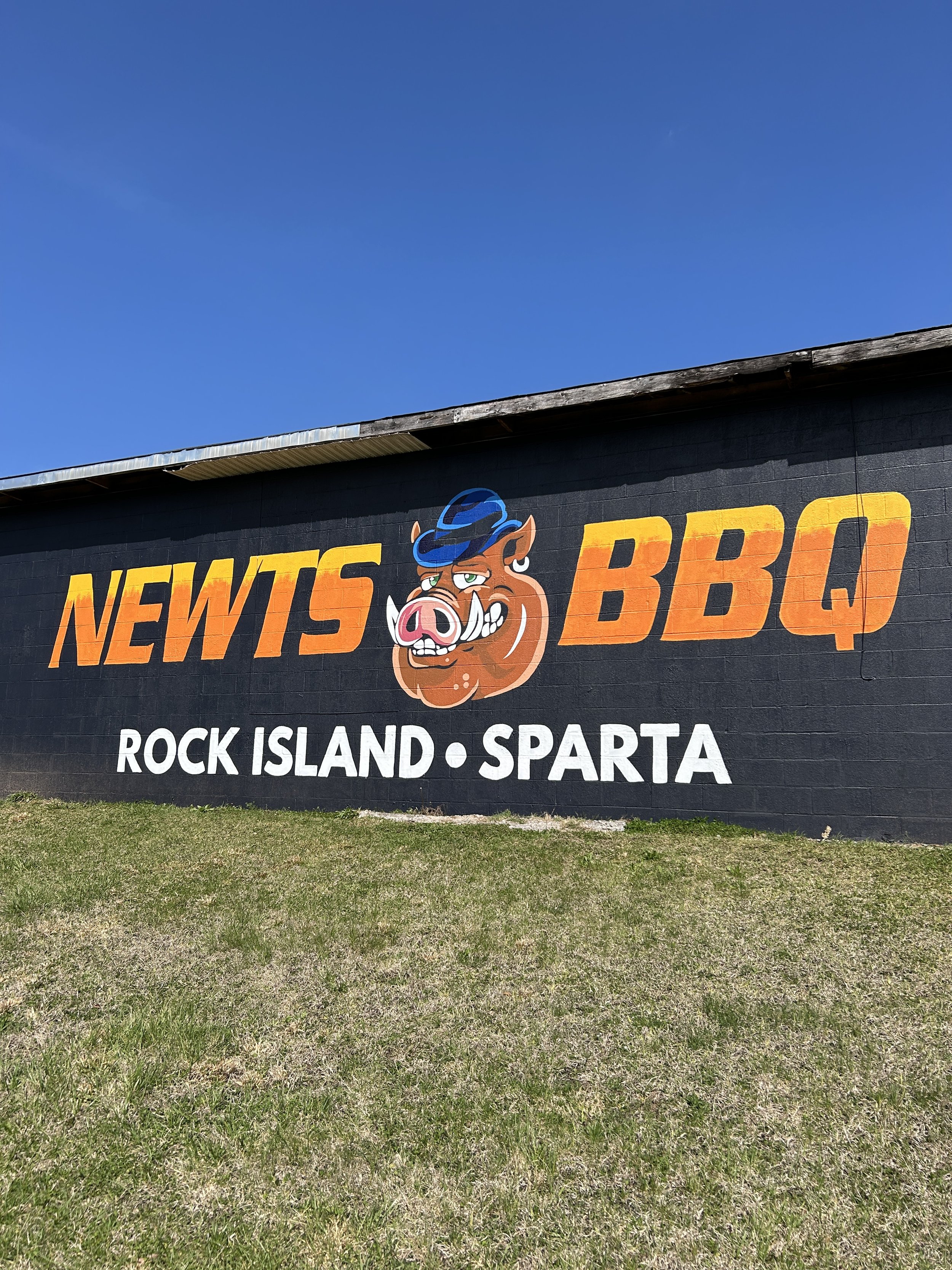 Wall mural advertising Newts BBQ in Rock Island, Sparta, featuring a cartoon pig wearing a blue hat.