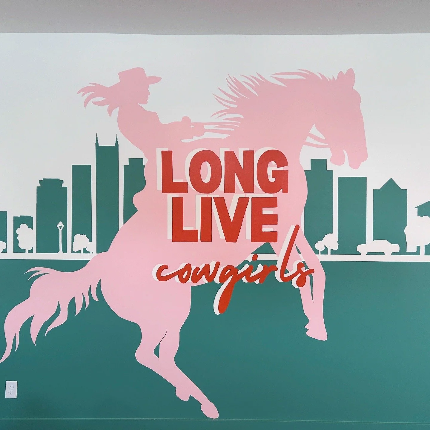 Airbnb Focal Wall with a pink silhouette of a woman riding a horse, city skyline background, and the text "Long Live Cowgirls" in bold and cursive fonts. Nashville, TN.