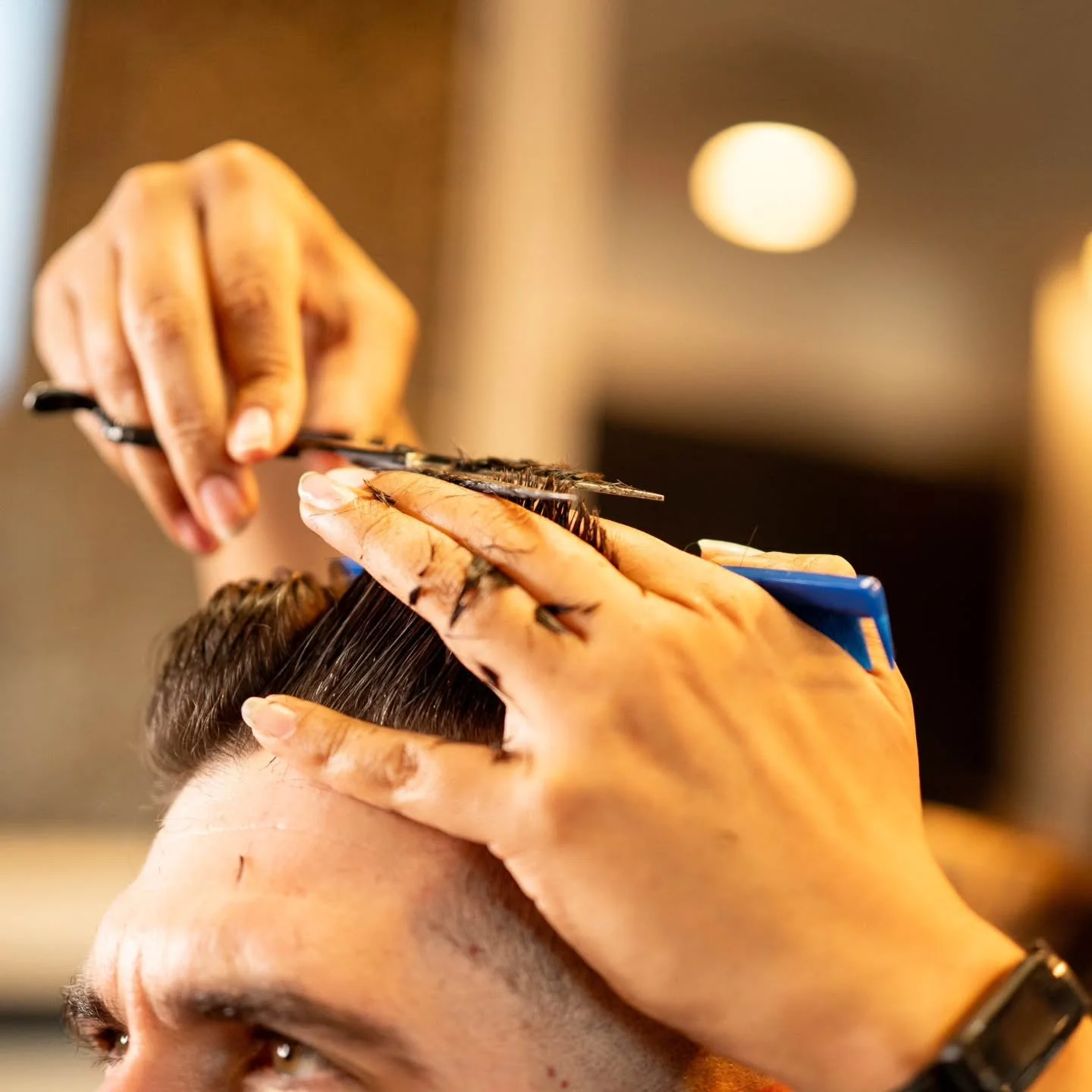 Close-up of scissors trimming damp hair held between a barber's fingers at Barbon's Barbershop.